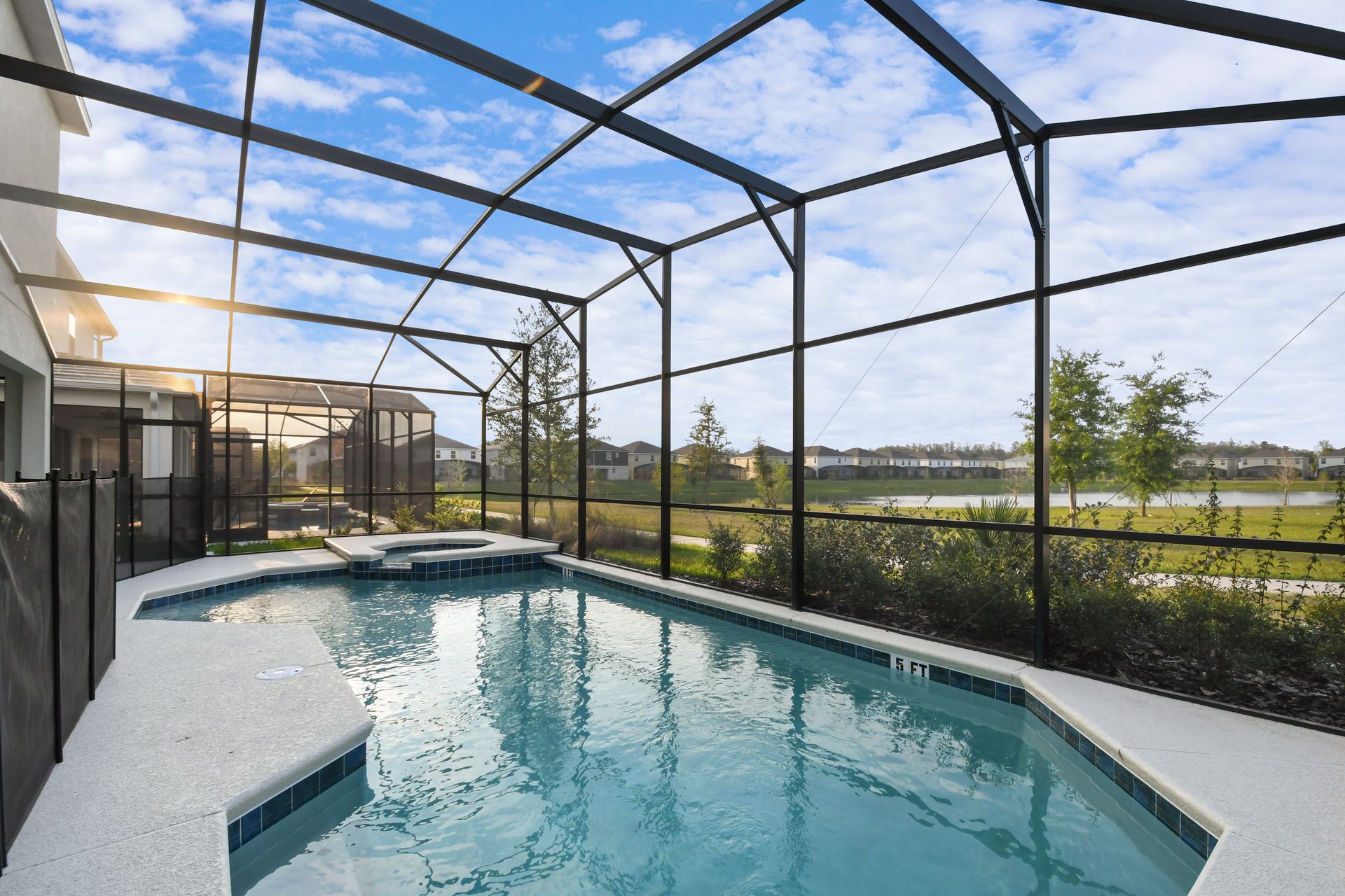 Screened-in pool with spa overlooking a serene lake and lush greenery.