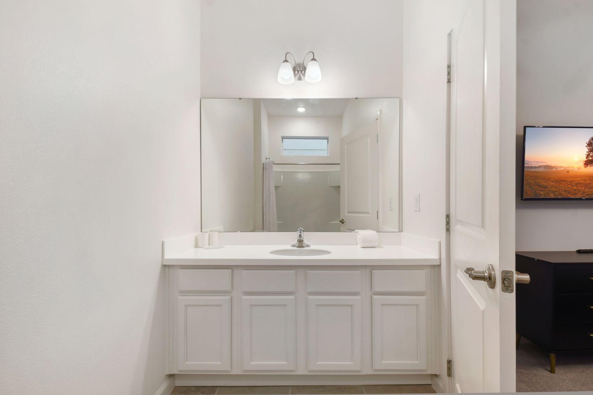 Bright bathroom with a large mirror, clean white cabinetry, and a spacious shower.