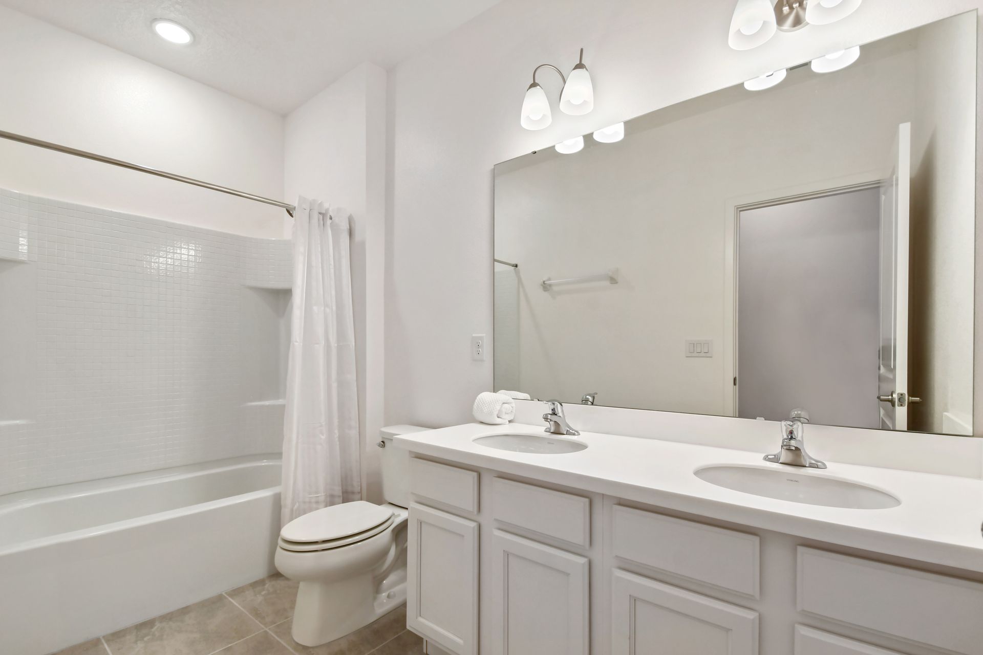 Bright bathroom with dual sinks, a large mirror, and a shower-tub combination.