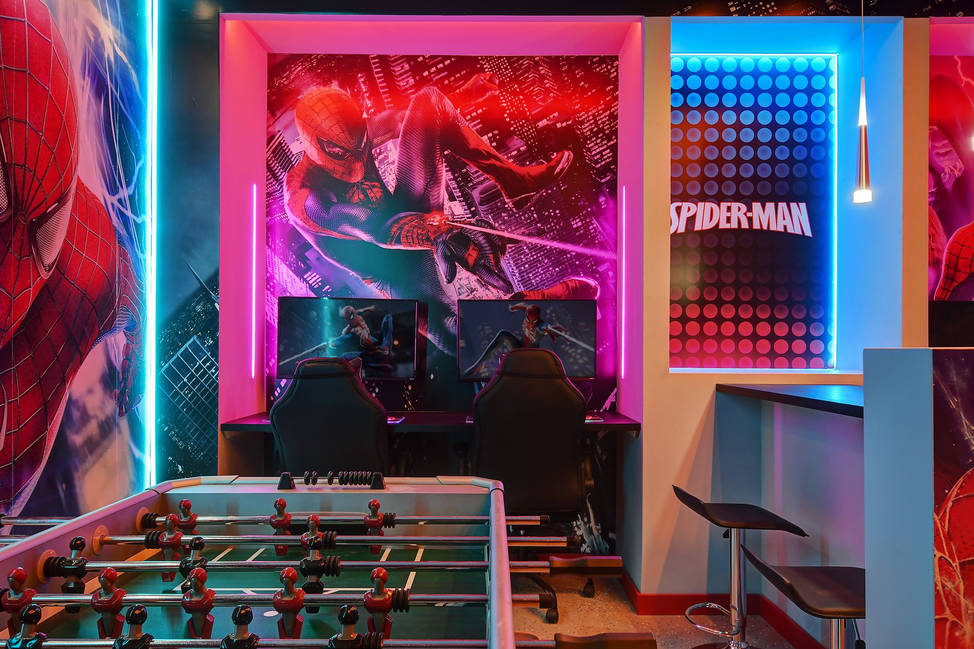 Spiderman-themed gaming station with dual monitors, neon lights, and foosball.