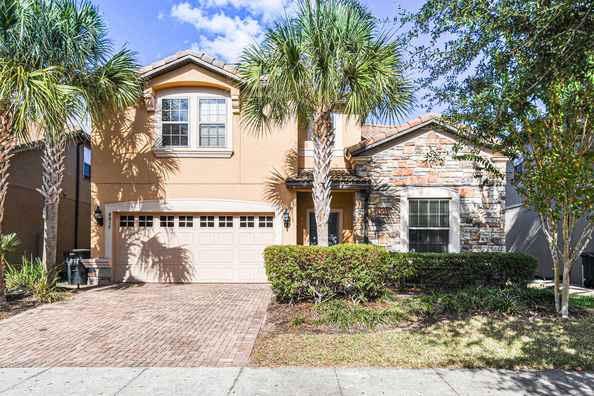 Beautiful villa with palm trees, stone accents, and spacious driveway in sunny setting.