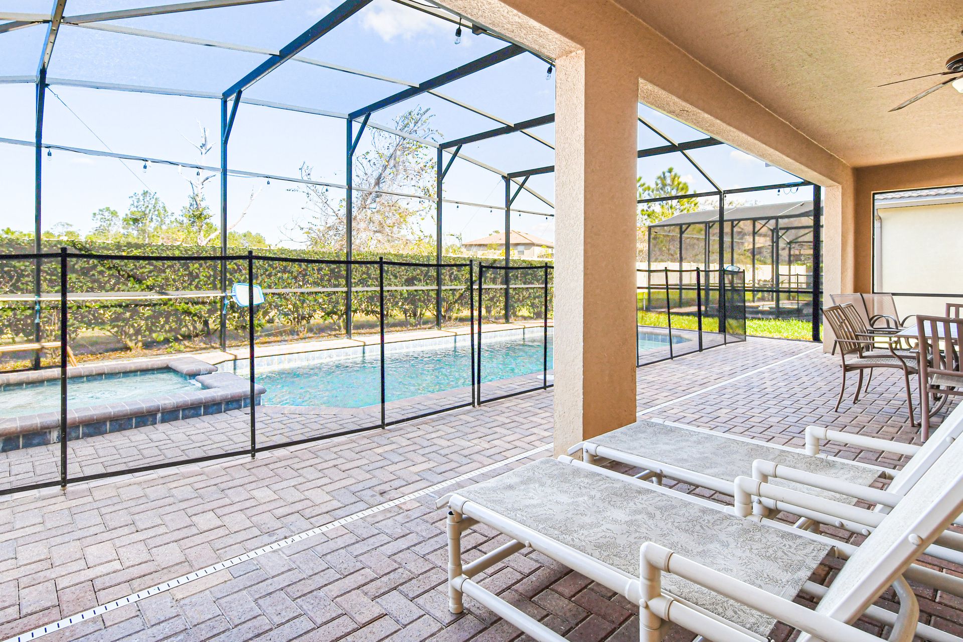 Covered patio with dining area, lounge chairs, ceiling fan, and screened pool view.