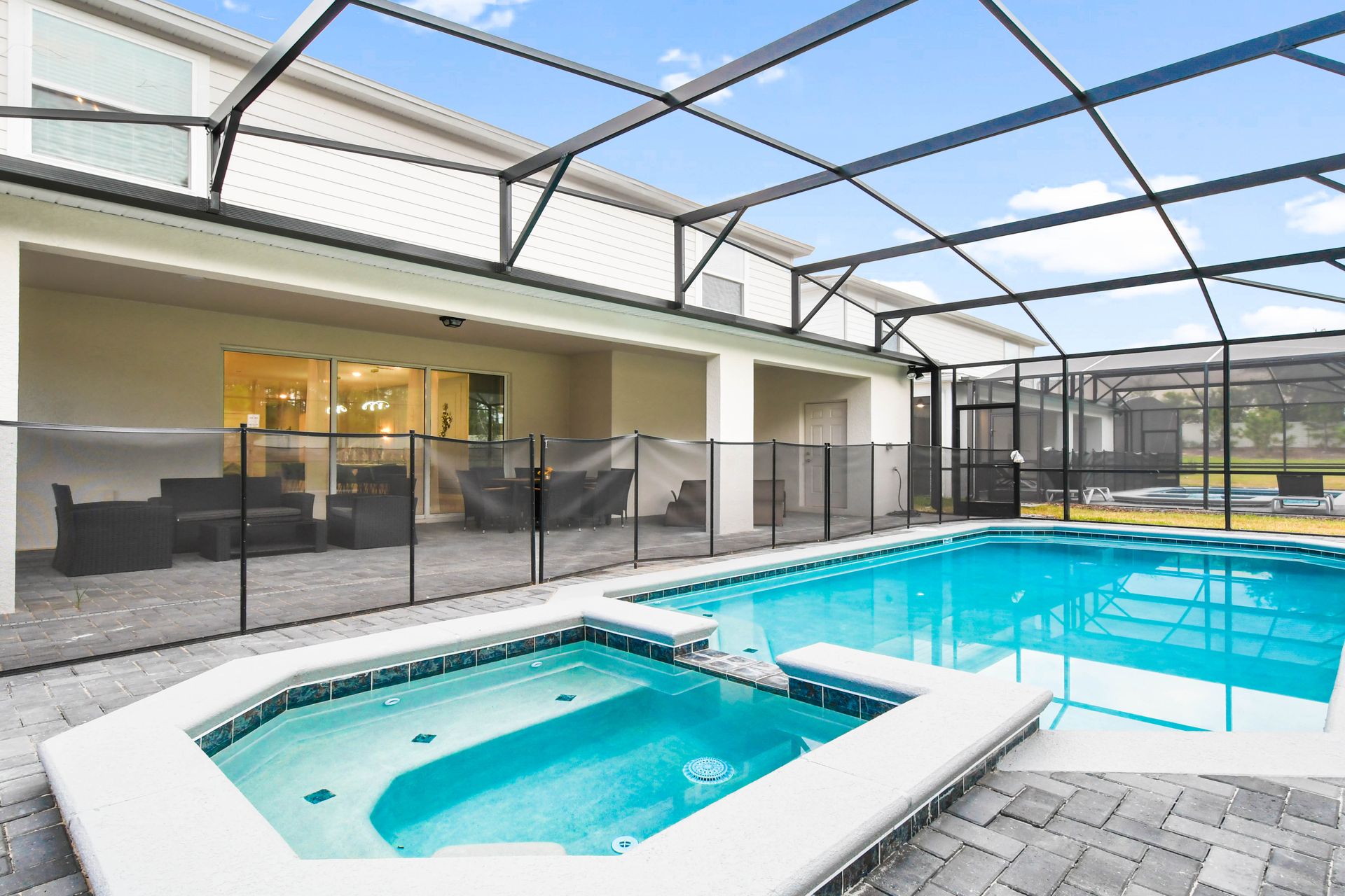 Private screened-in pool and spa with patio seating, safety fence, and sunny views.