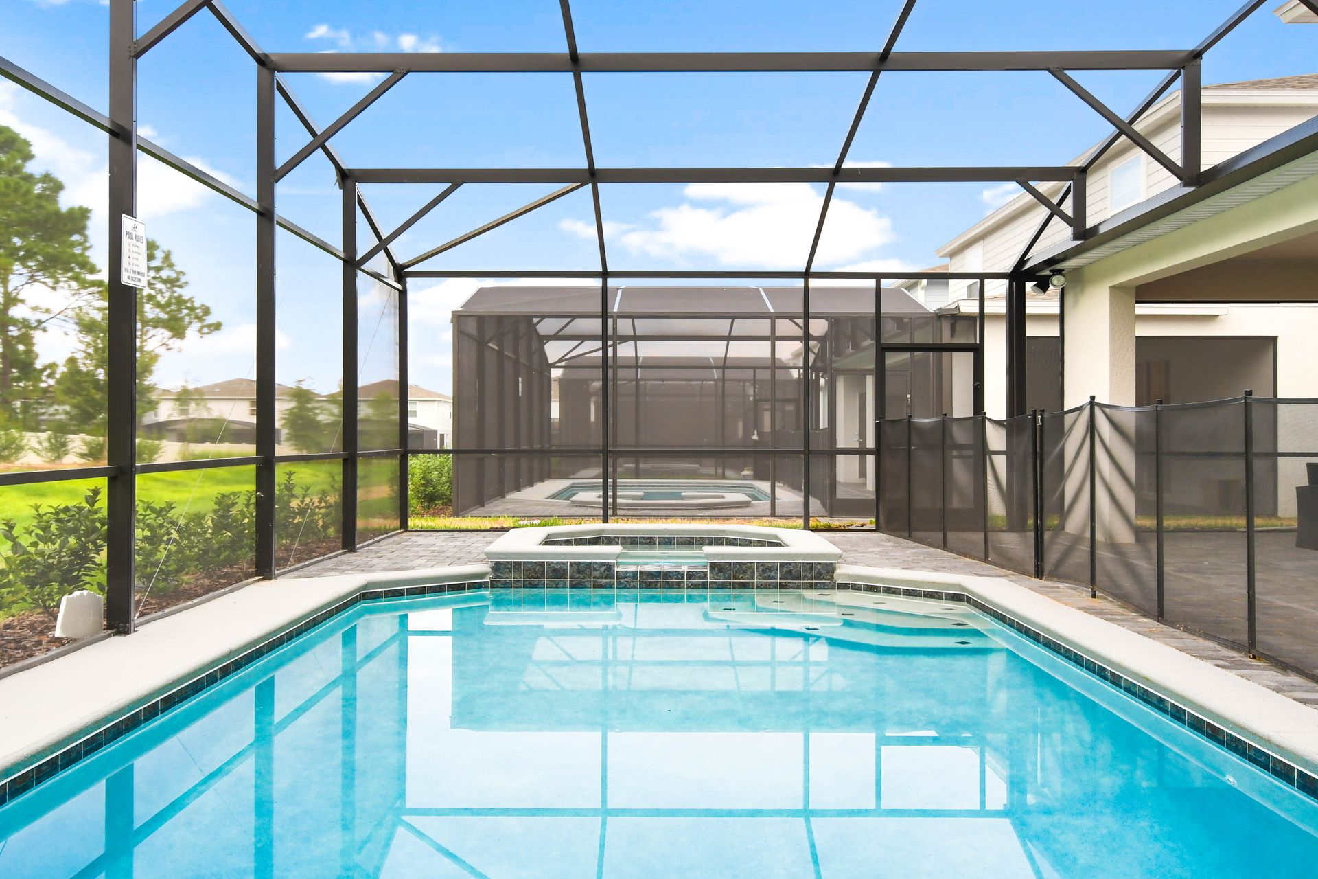 Private screened-in pool and spa with patio seating, safety fence, and sunny views.