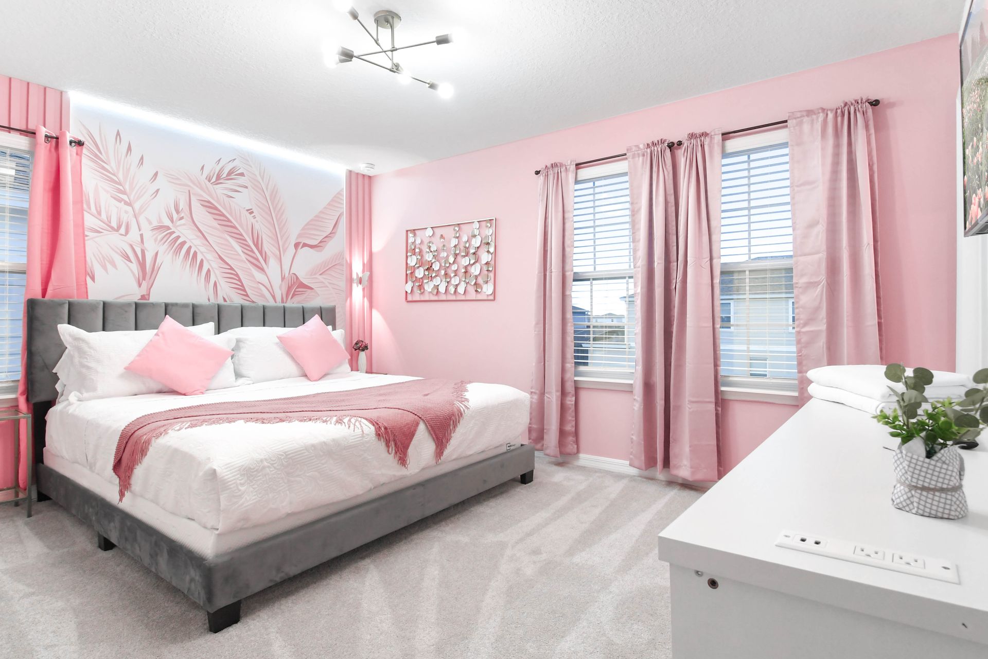 Chic pink bedroom with a king bed, soft tones, and stylish tropical wall art.