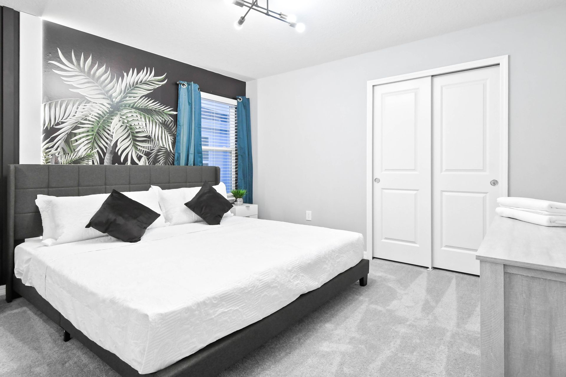 Modern monochrome bedroom with tropical wall art, king bed, and sleek decor.
