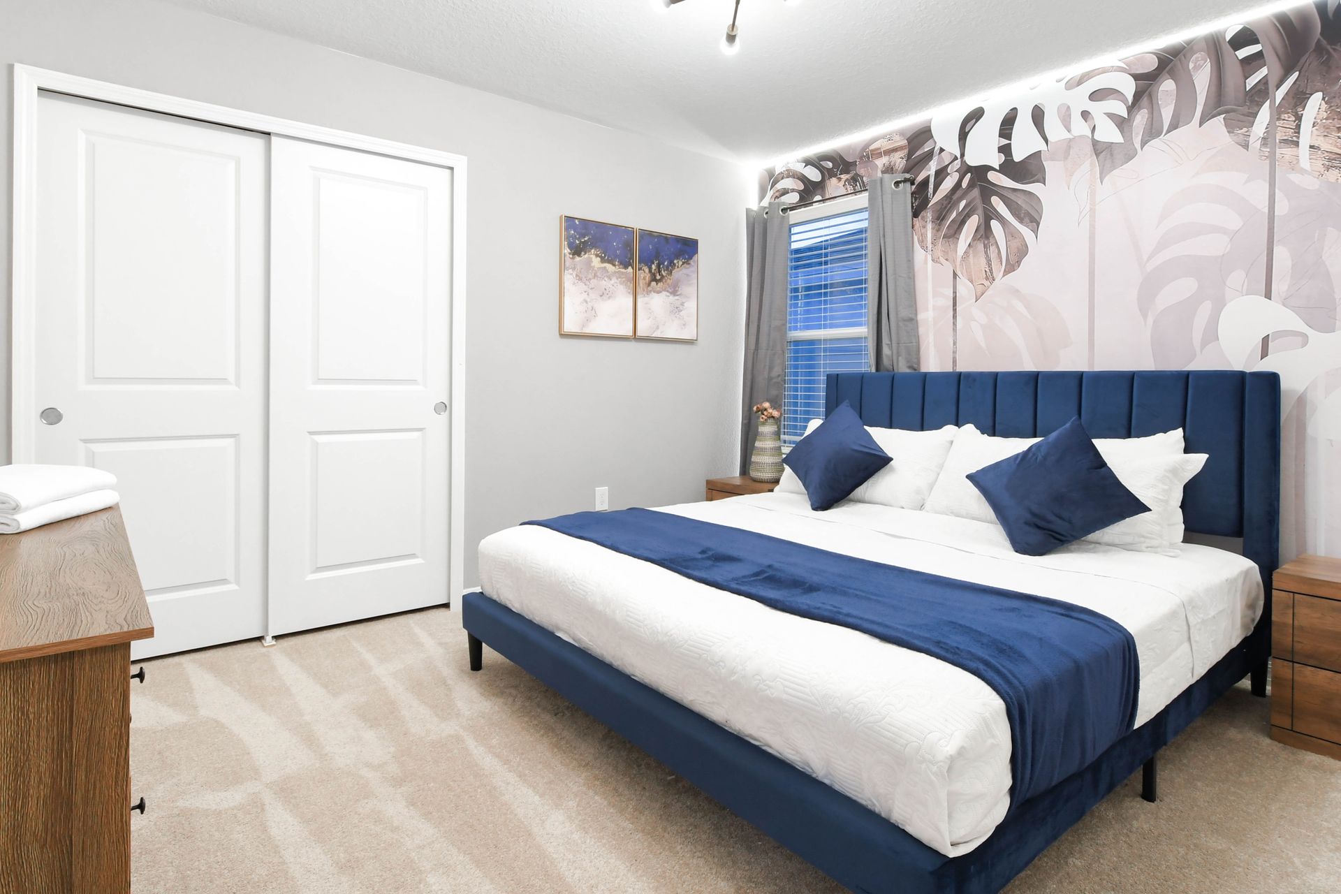 Elegant bedroom with king bed, deep blue accents, and tropical wall design.