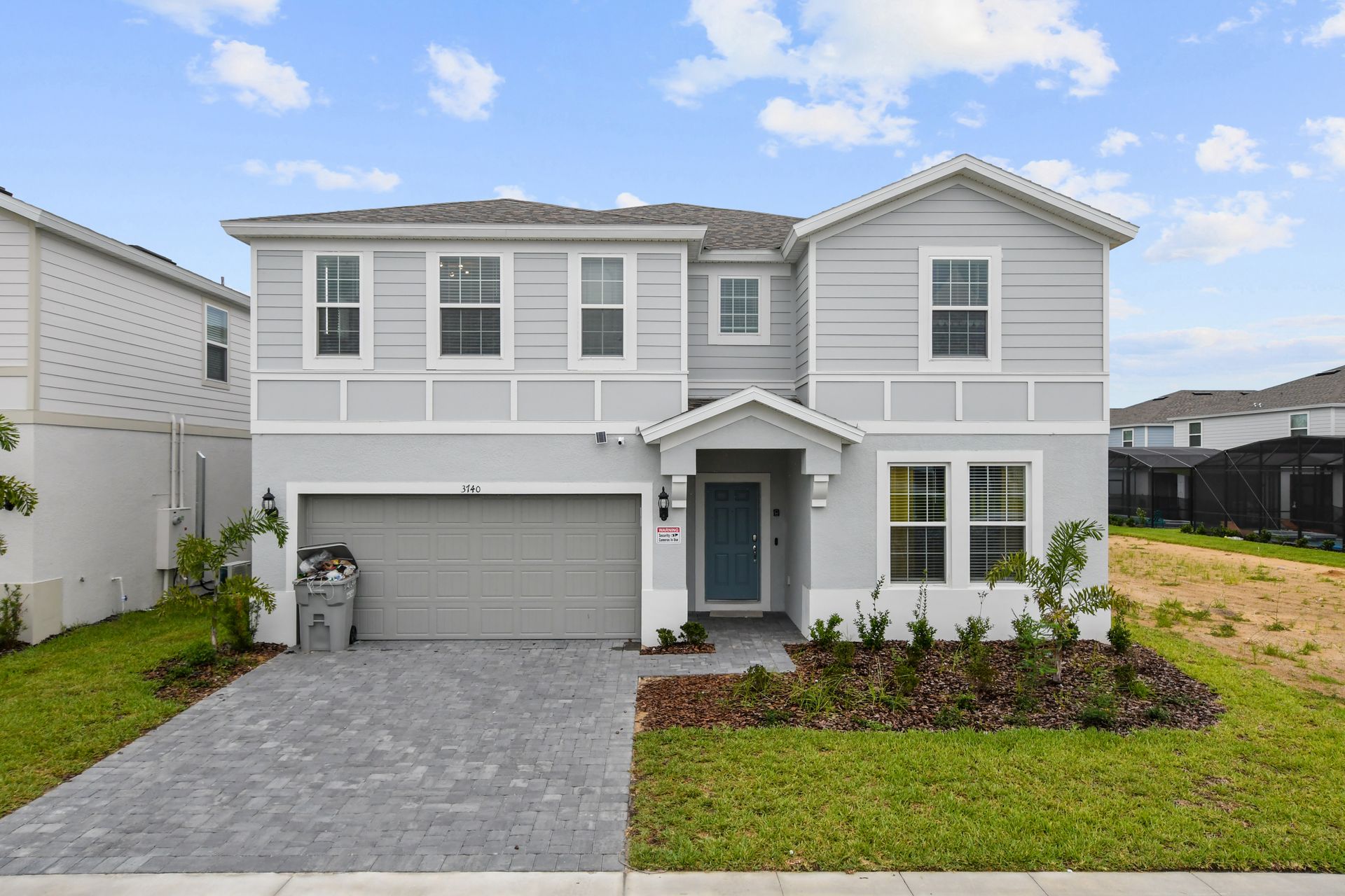 Modern two-story home with sleek gray siding, a blue front door, and a private screened-in pool.