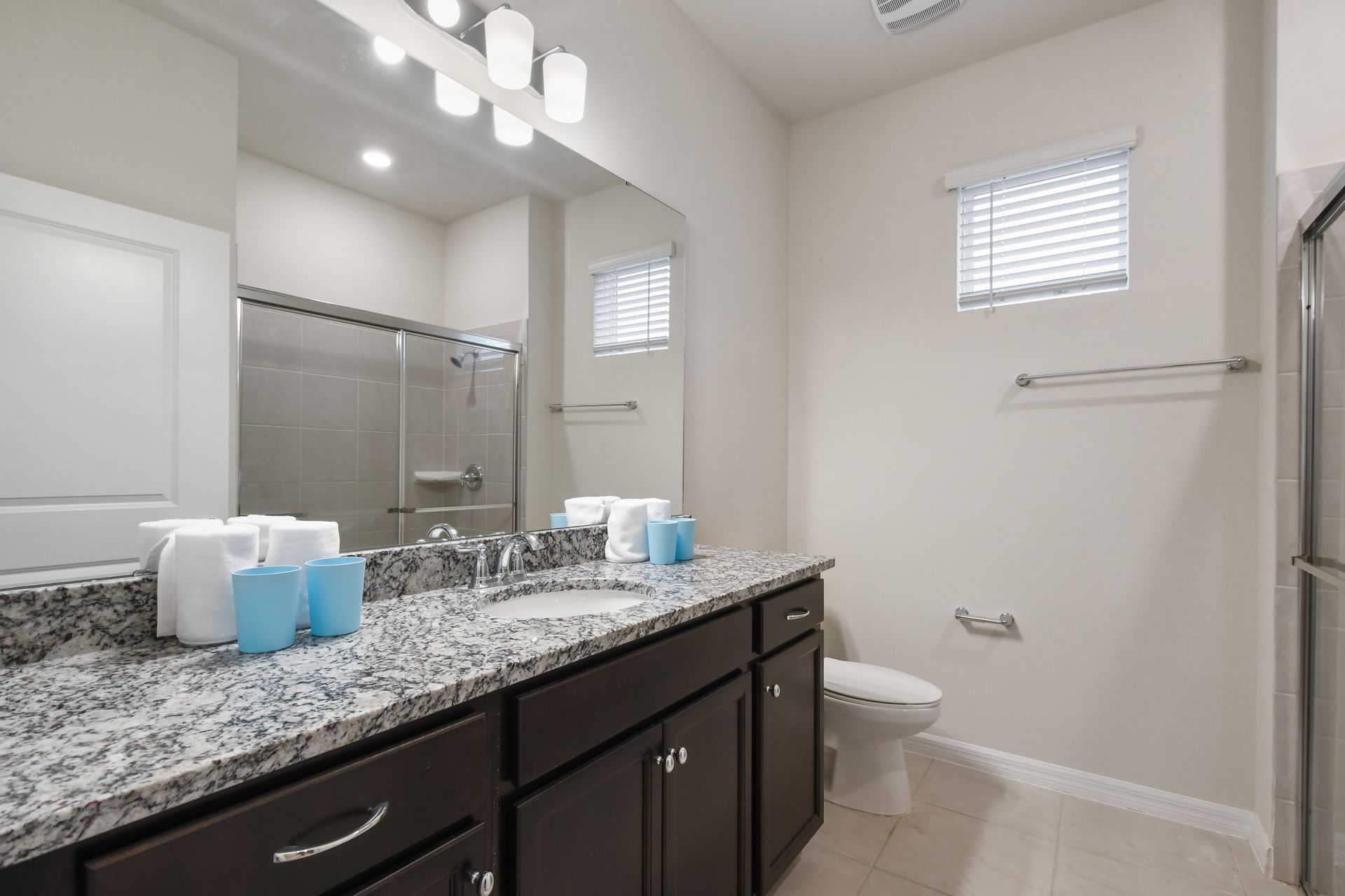 Bright bathroom with granite counters, double sinks, and a walk-in glass shower.