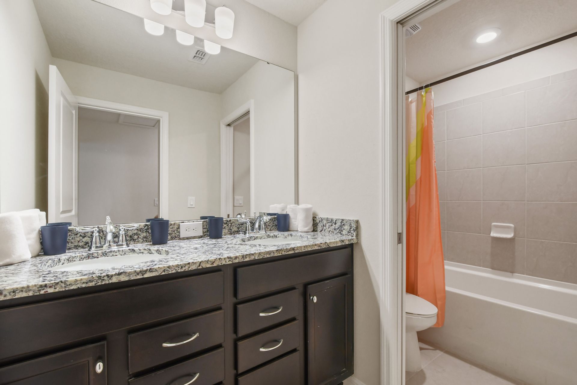 Modern bathroom with dual sinks, granite counters, and a tub-shower combo.