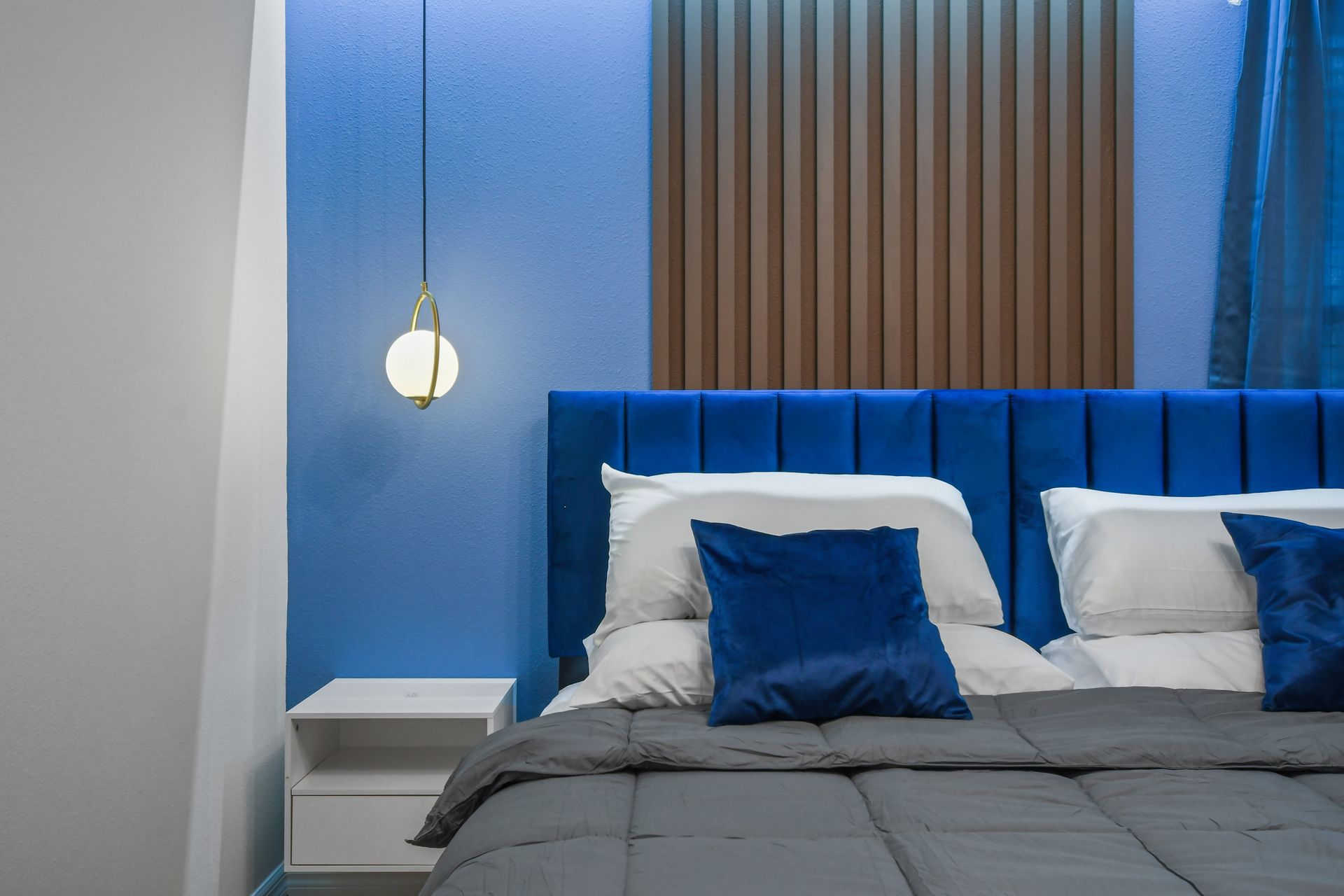 Luxurious blue velvet headboard, glowing accent wall, and elegant hanging light.