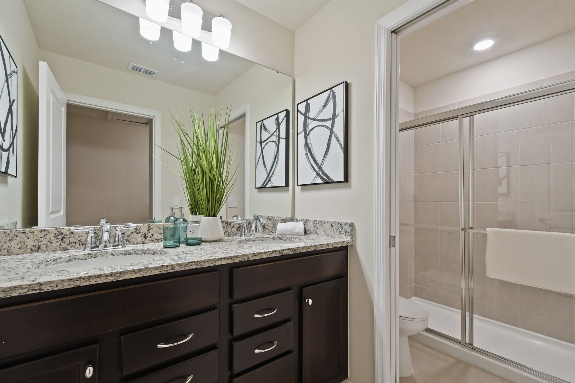 Stylish bathroom with granite double vanity, glass shower, modern art and lighting
