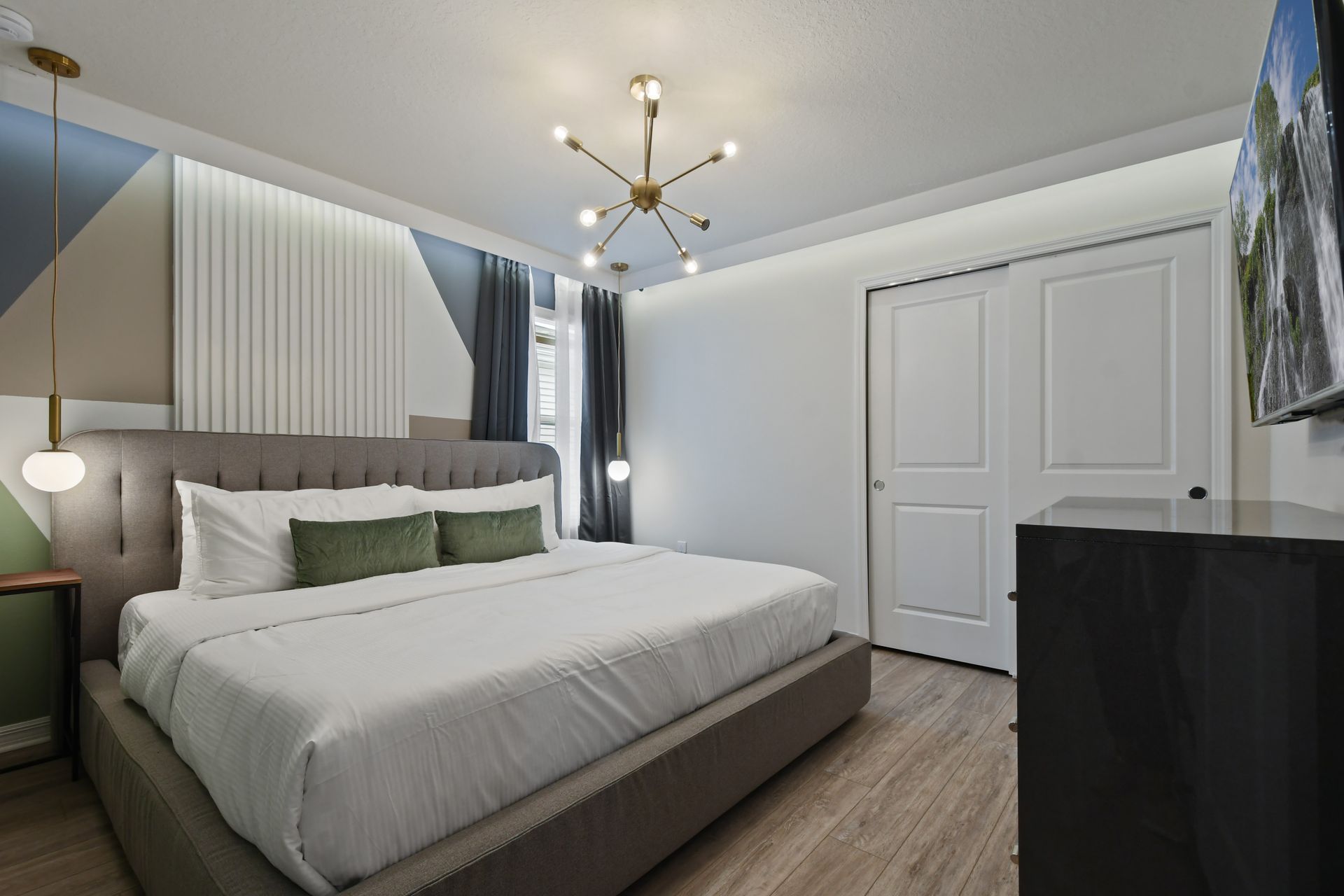 Modern king bedroom with stylish lighting, cozy bed, geometric accent wall, and TV
