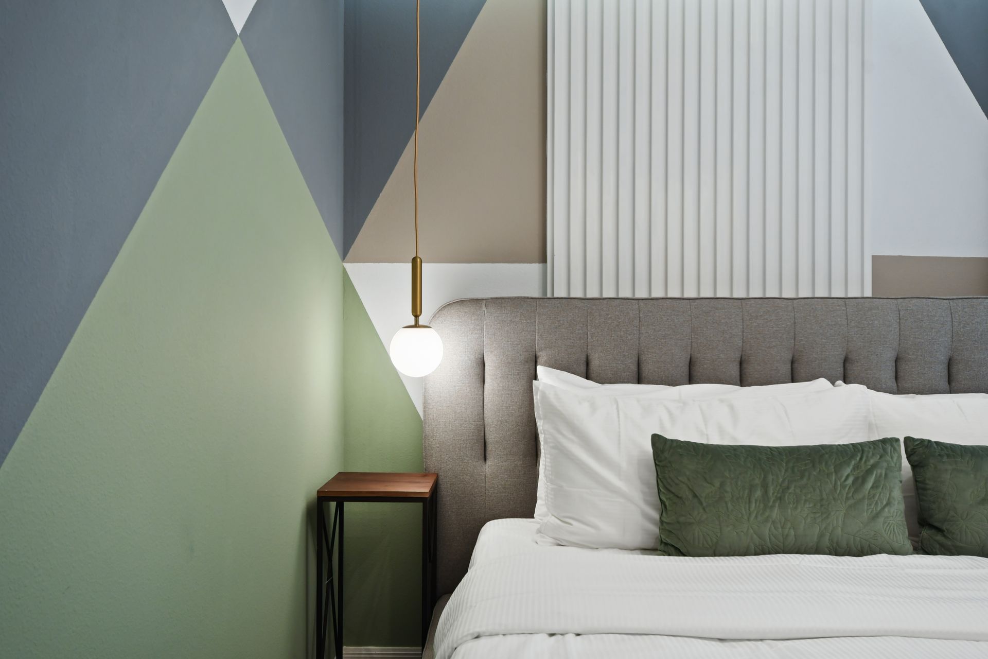 Modern king bedroom with stylish lighting, cozy bed, geometric accent wall, and TV
