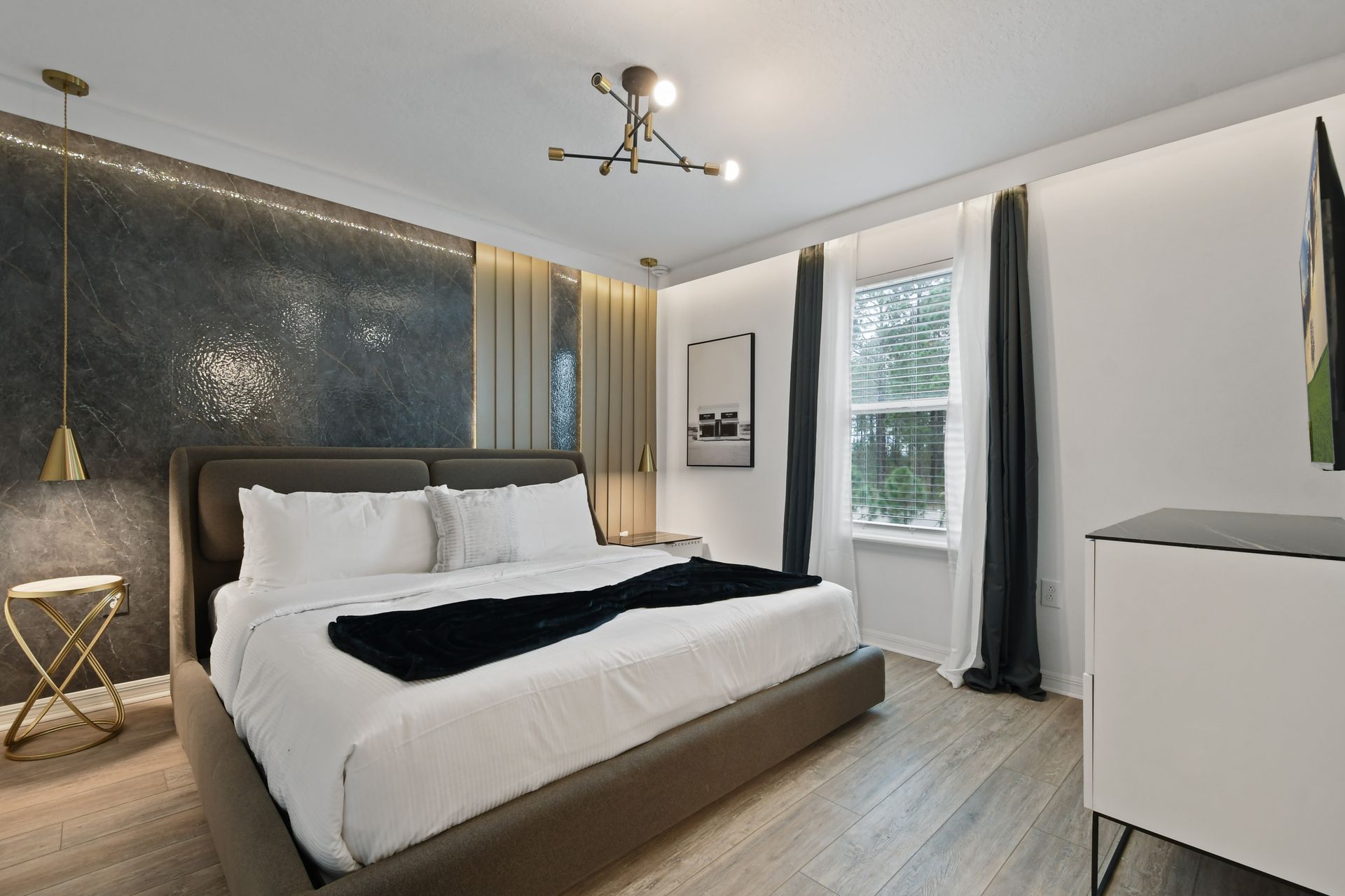 Elegant modern bedroom with king bed, chic accent wall, gold lighting, and TV
