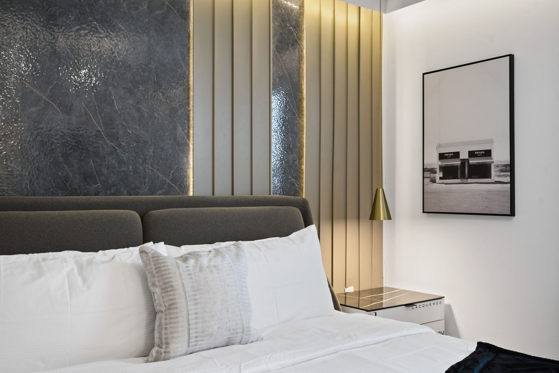 Luxurious king bedroom with textured accent wall, gold pendant light, and plush bedding
