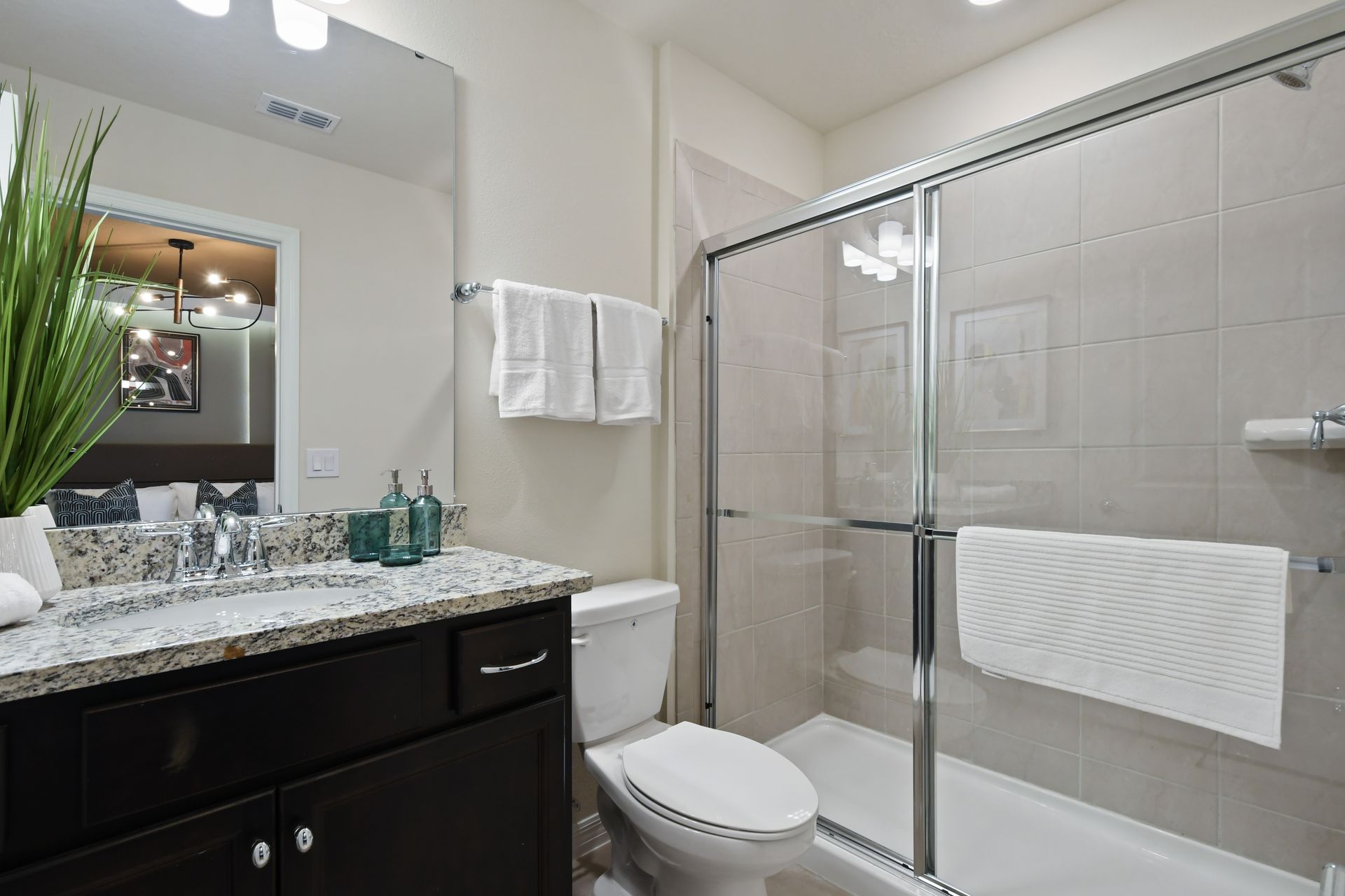 Modern bathroom with granite vanity, glass shower, plush towels, and fresh decor
