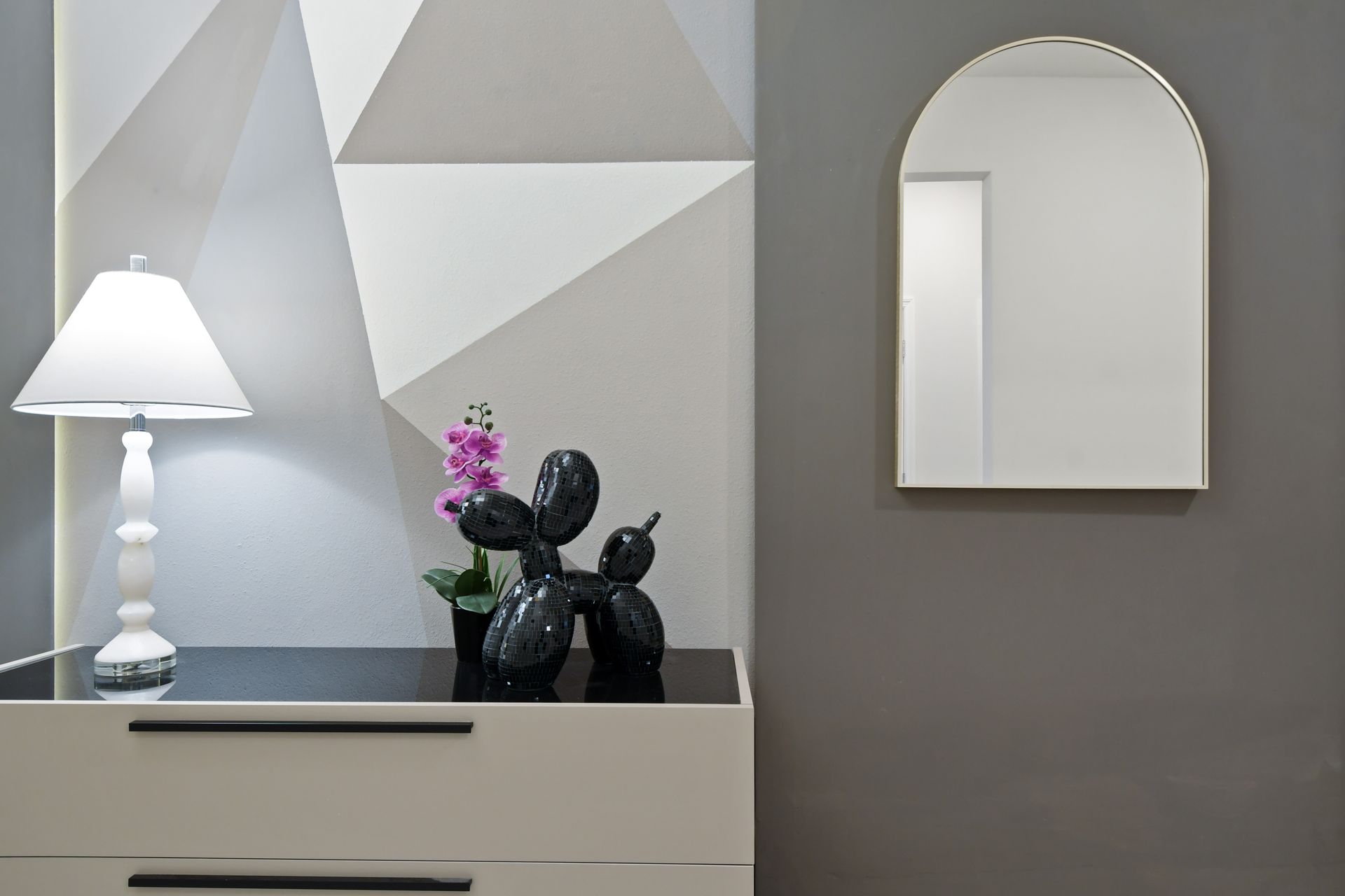 Chic entry table with geometric wall, modern lamp, playful decor, orchid, and mirror
