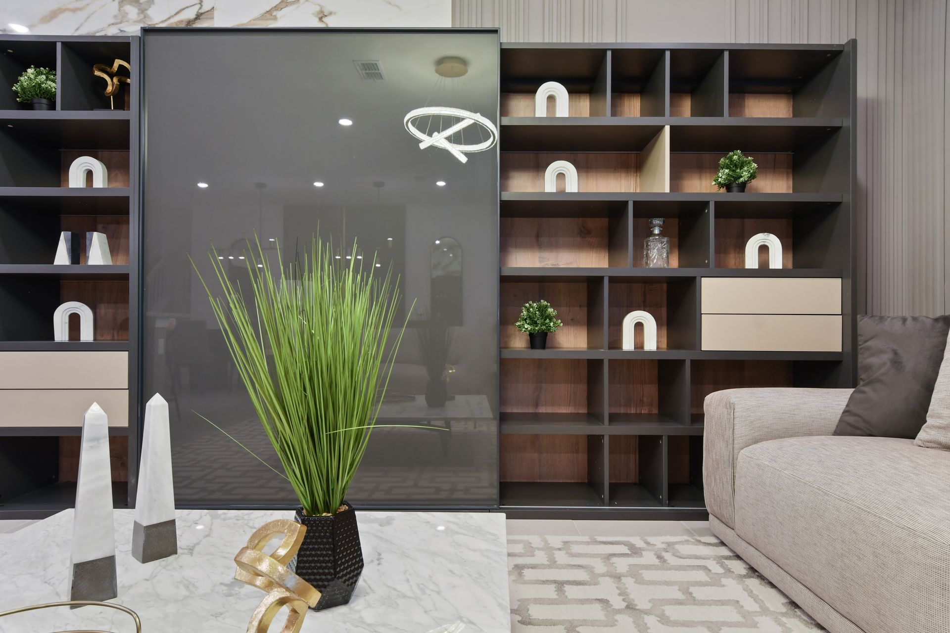 Modern living room detail featuring built-in shelving with decorative pieces, a partial glass room divider, a marble coffee table with stylish decor, and a cozy beige sofa.

