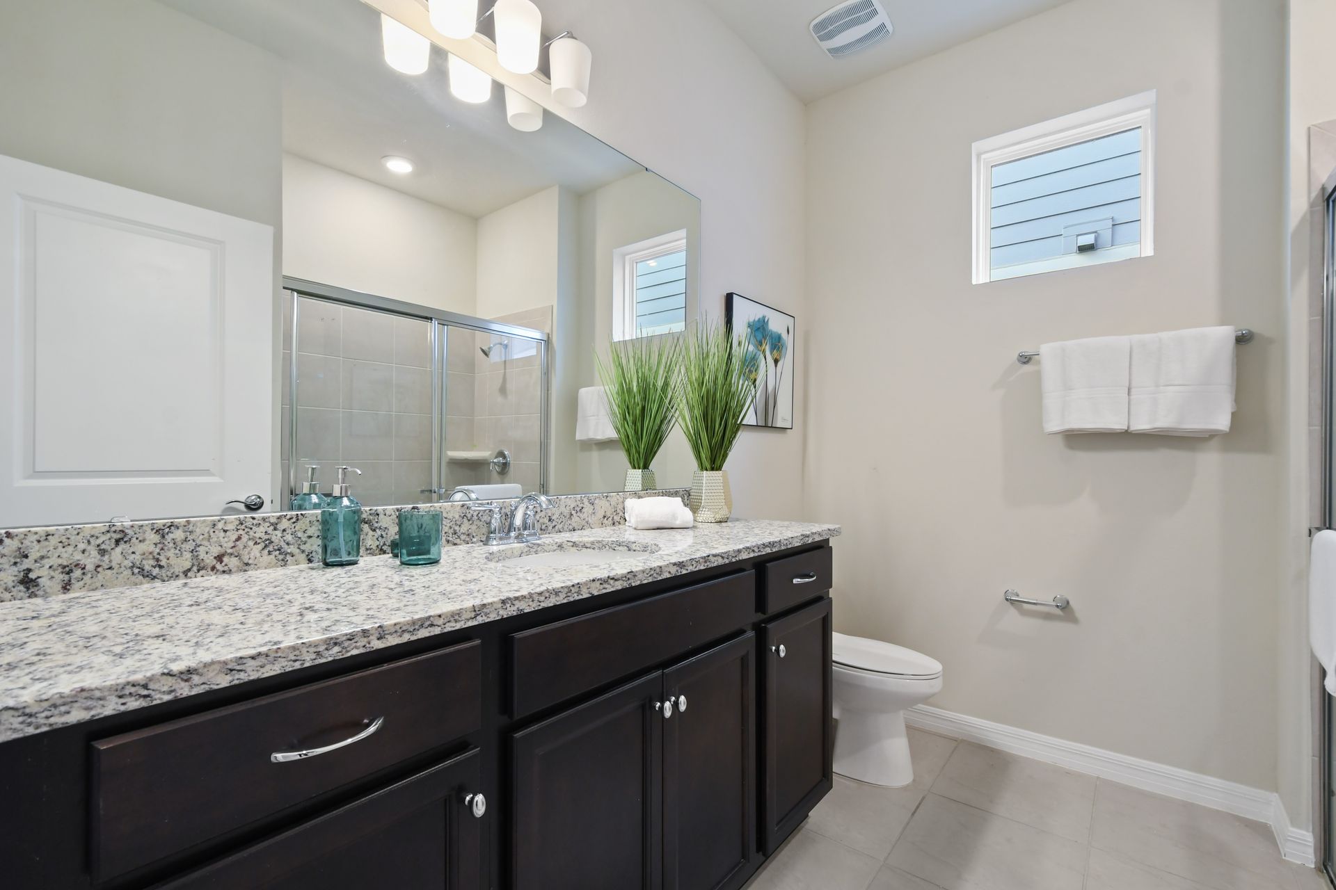 Bright bathroom with granite double vanity, glass shower, modern fixtures, and decor
