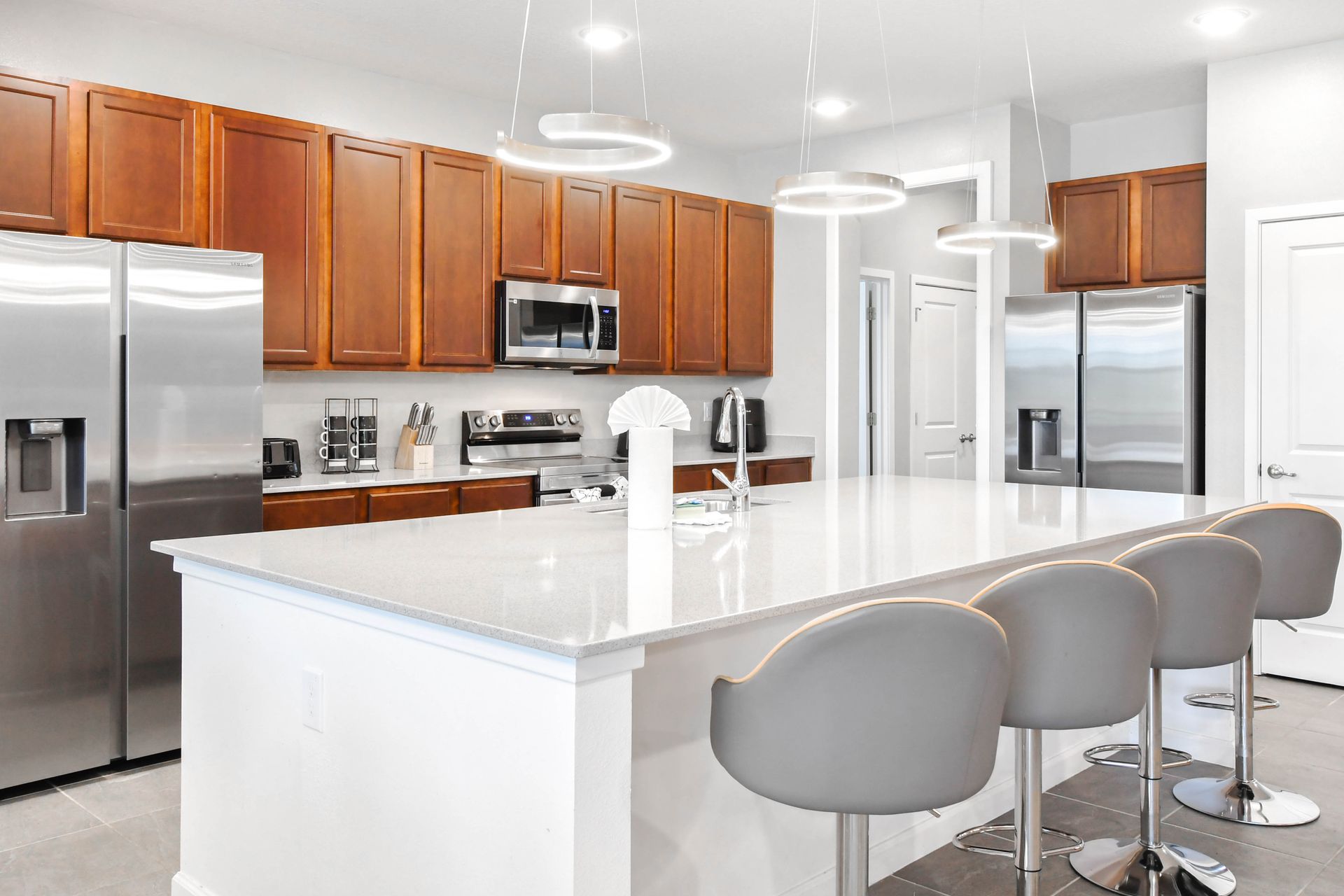 Modern kitchen with double fridges, sleek island seating, and stainless steel.