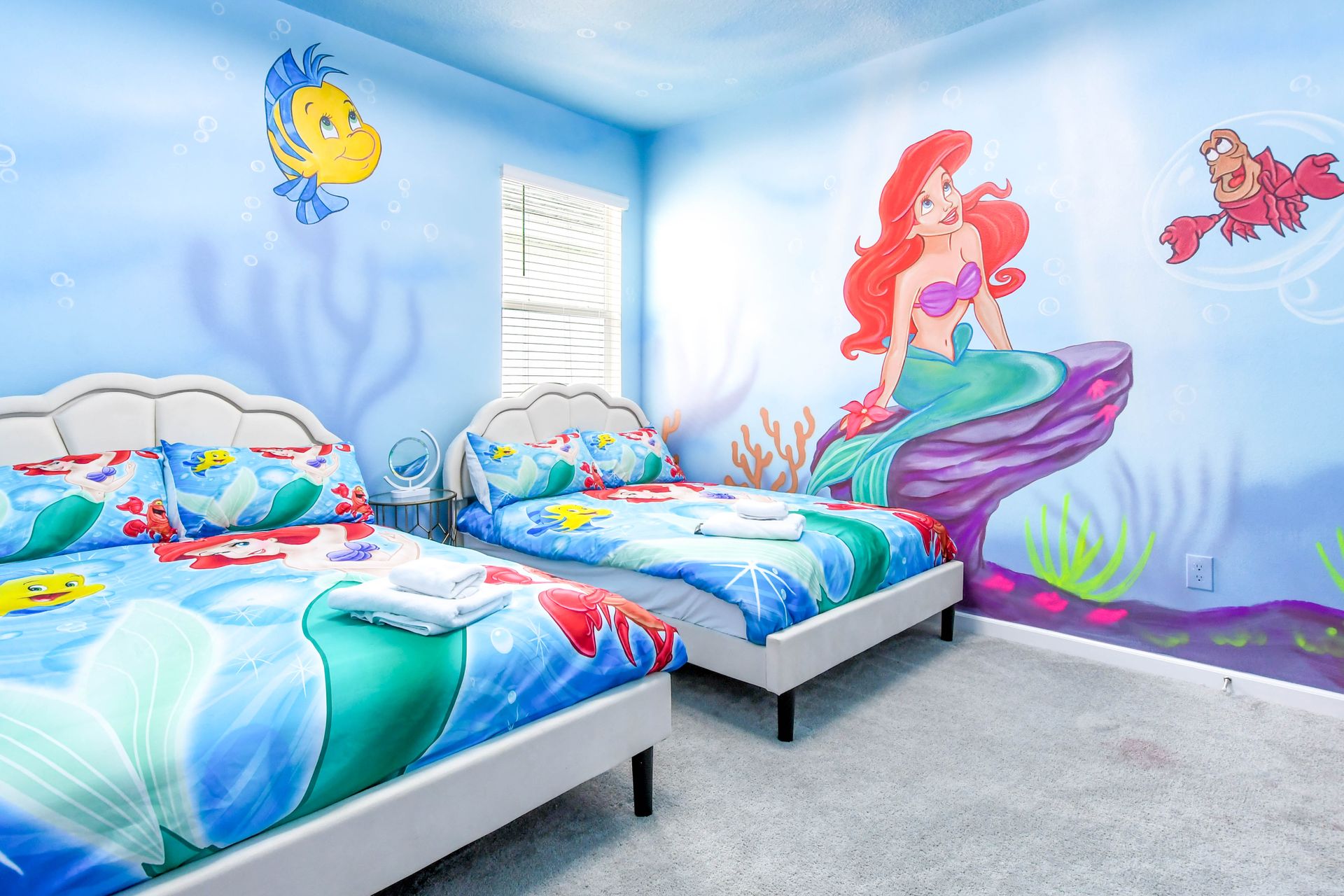 Little Mermaid-themed kids’ room with twin beds, vibrant murals, and ocean vibes.