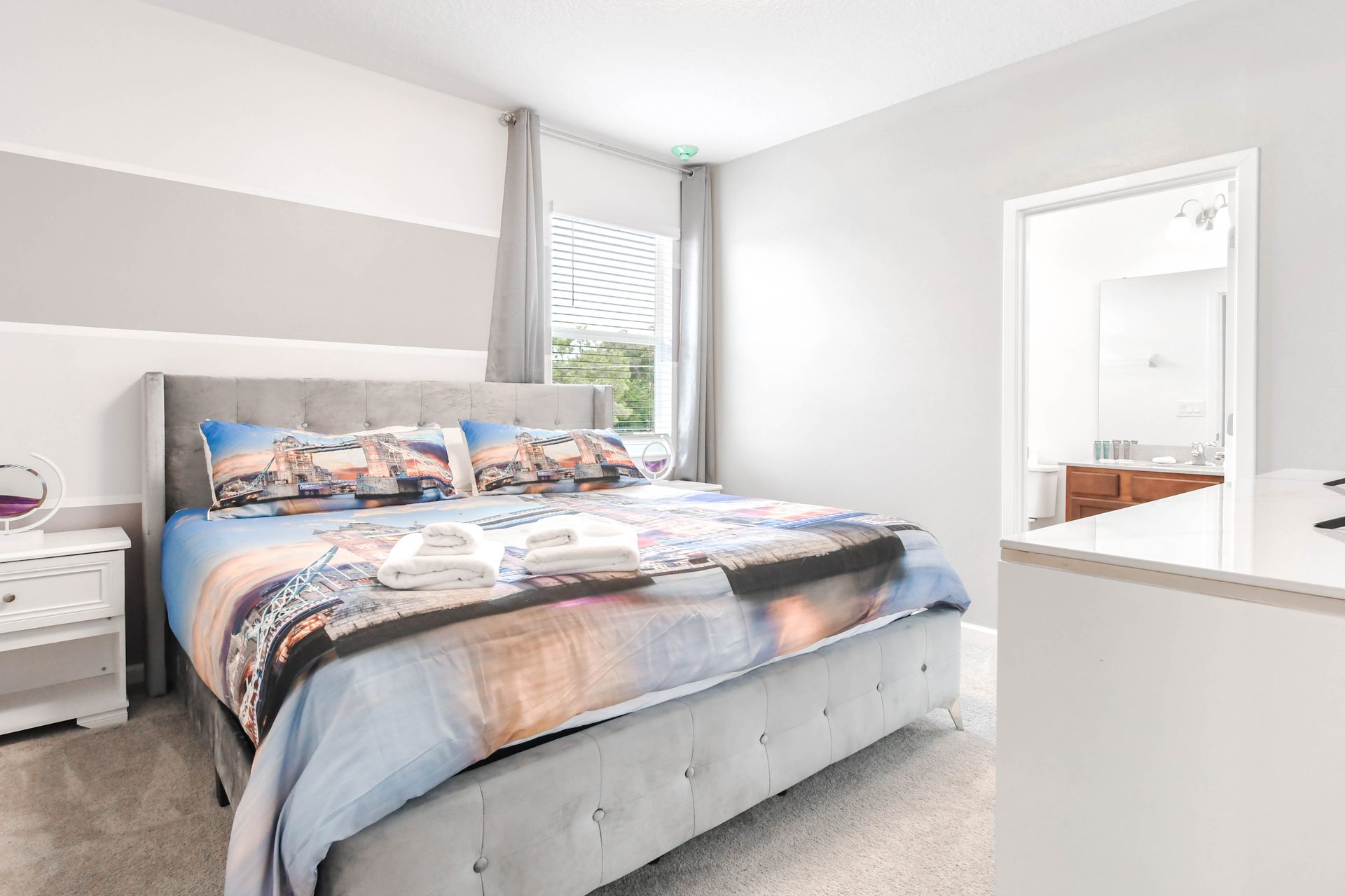 Modern king bedroom with cityscape bedding, neutral tones, and attached bathroom.