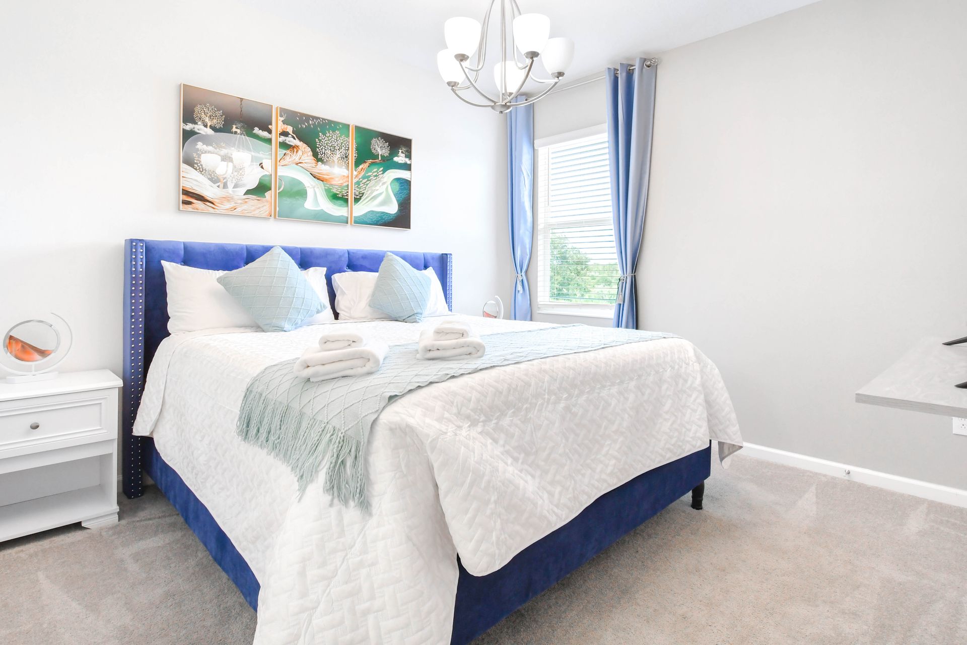 Elegant king bedroom with blue accents, soft bedding, and natural sunlight.