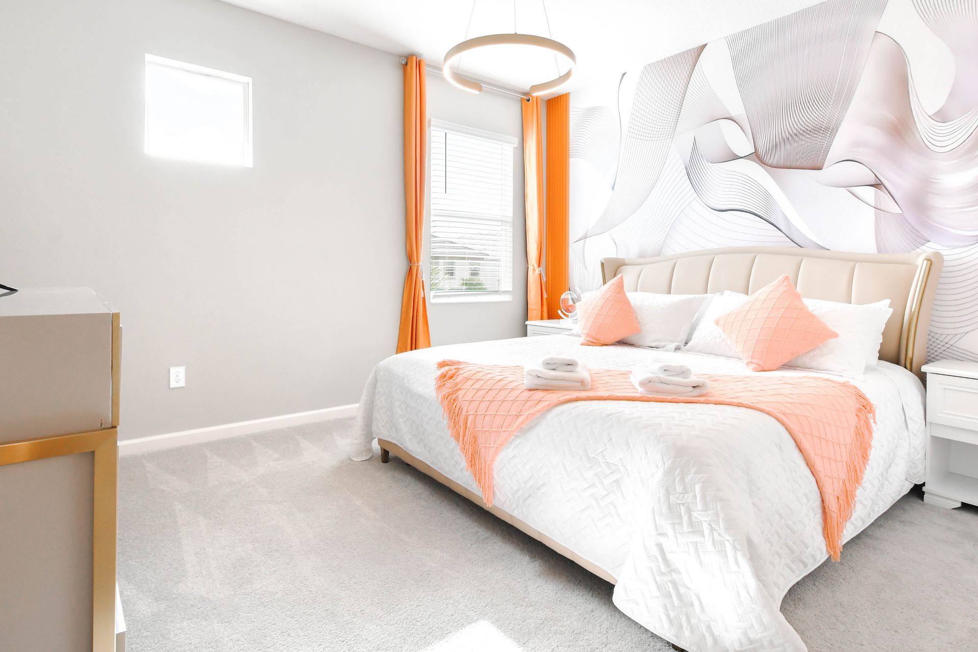 Bright modern bedroom with king bed, abstract accent wall, and bold orange decor.