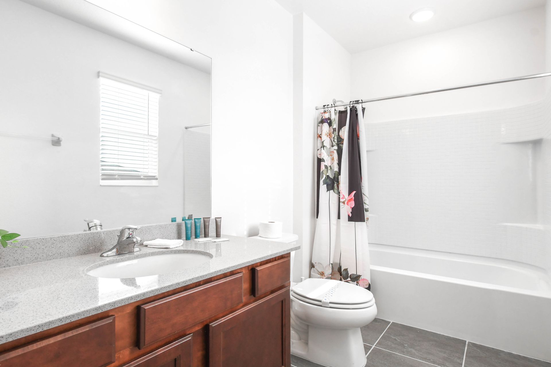 Bright bathroom with single sink, floral shower curtain, and large window.