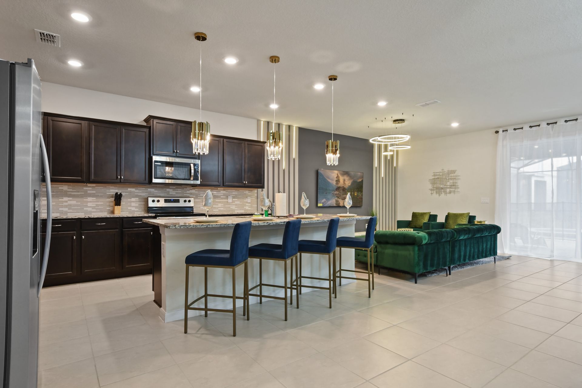Stylish kitchen with granite island, gold lighting, and open flow to luxe lounge.
