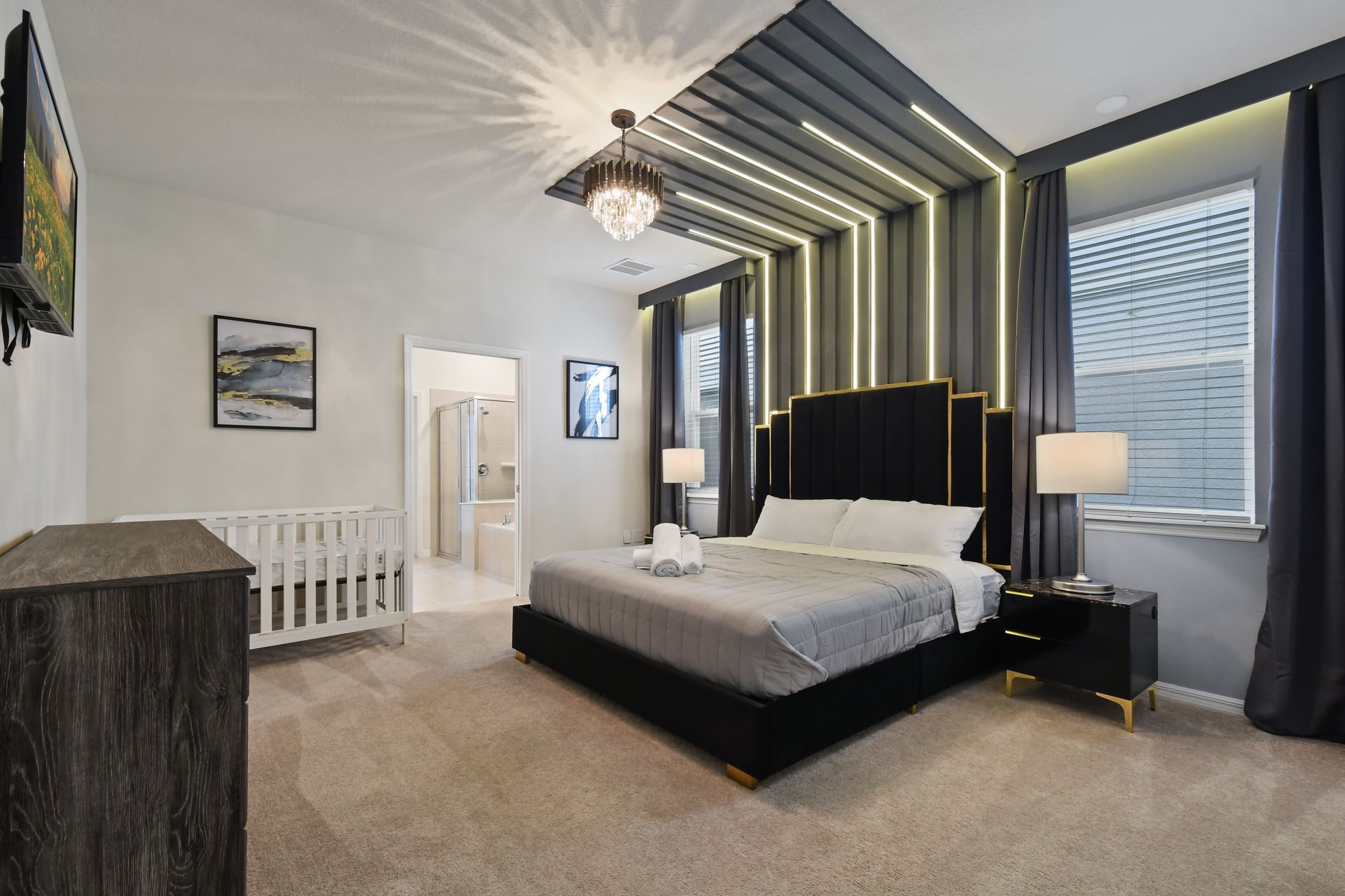 Modern king suite with dramatic lighting, crystal chandelier, and cozy crib corner.
