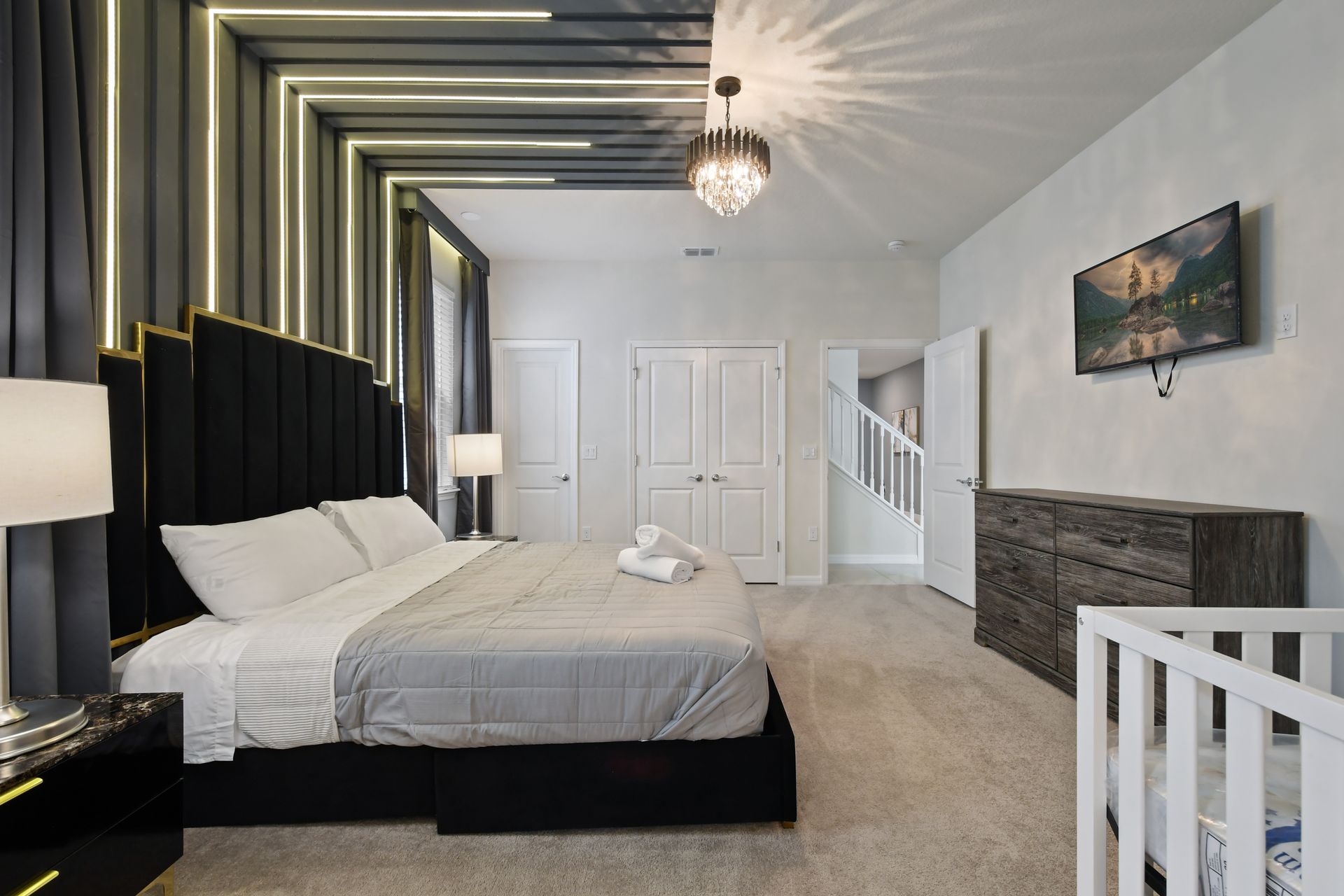 Modern king suite with dramatic lighting, crystal chandelier, and cozy crib corner.
