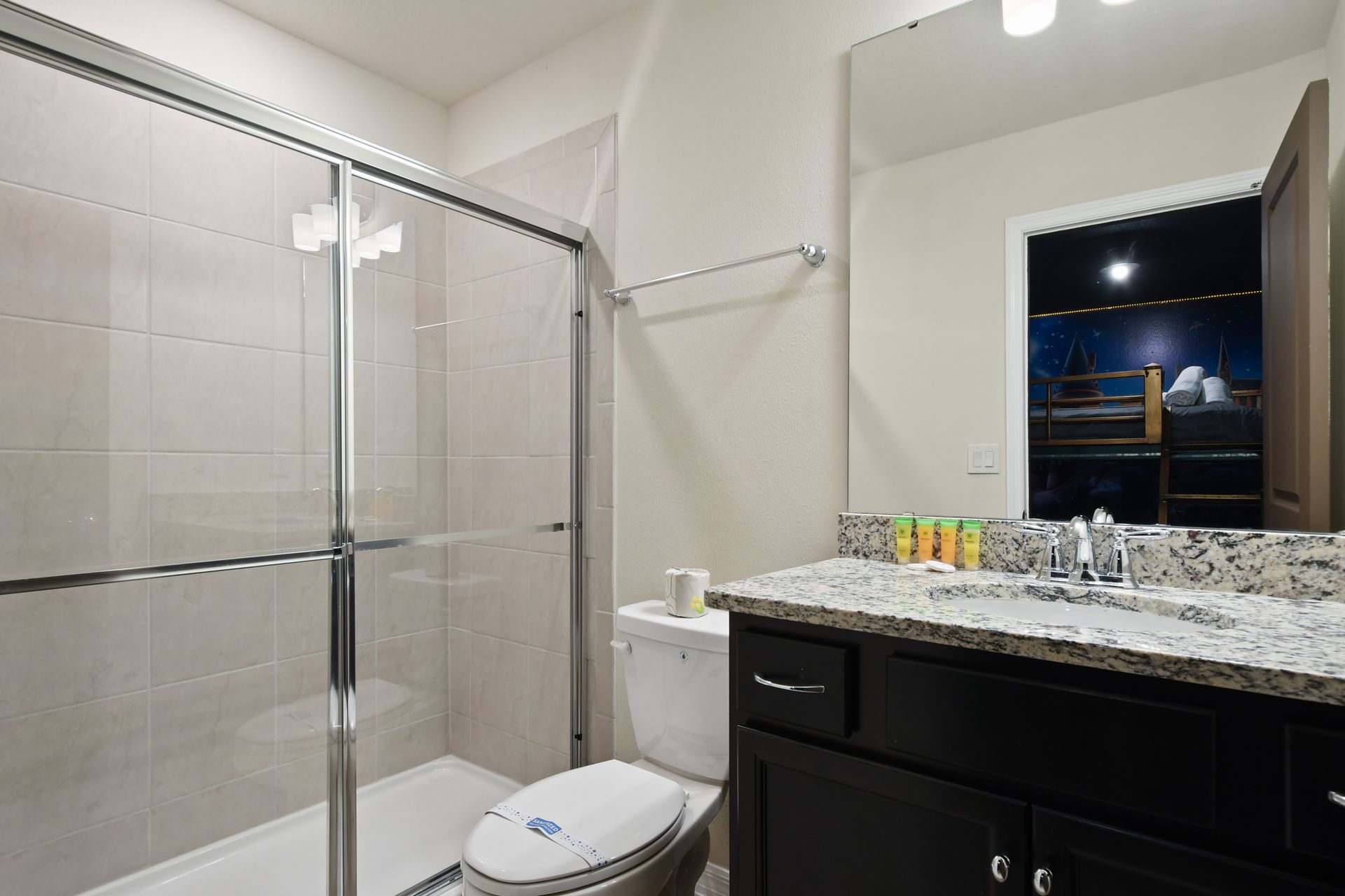 Modern bathroom with granite vanity, glass shower, and access to themed bedroom.
