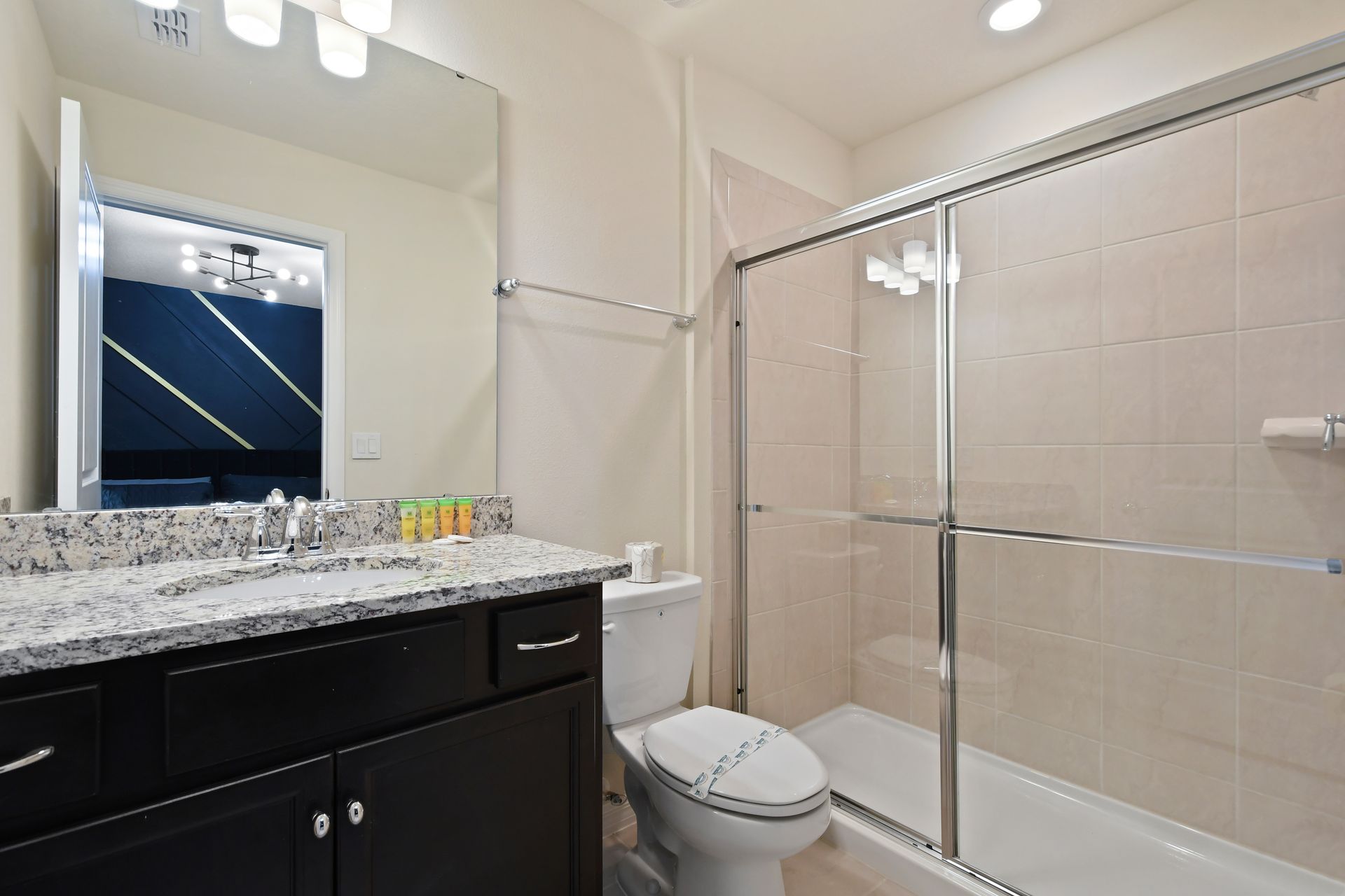 Modern bathroom with sleek granite vanity, glass shower, and soft recessed lighting.
