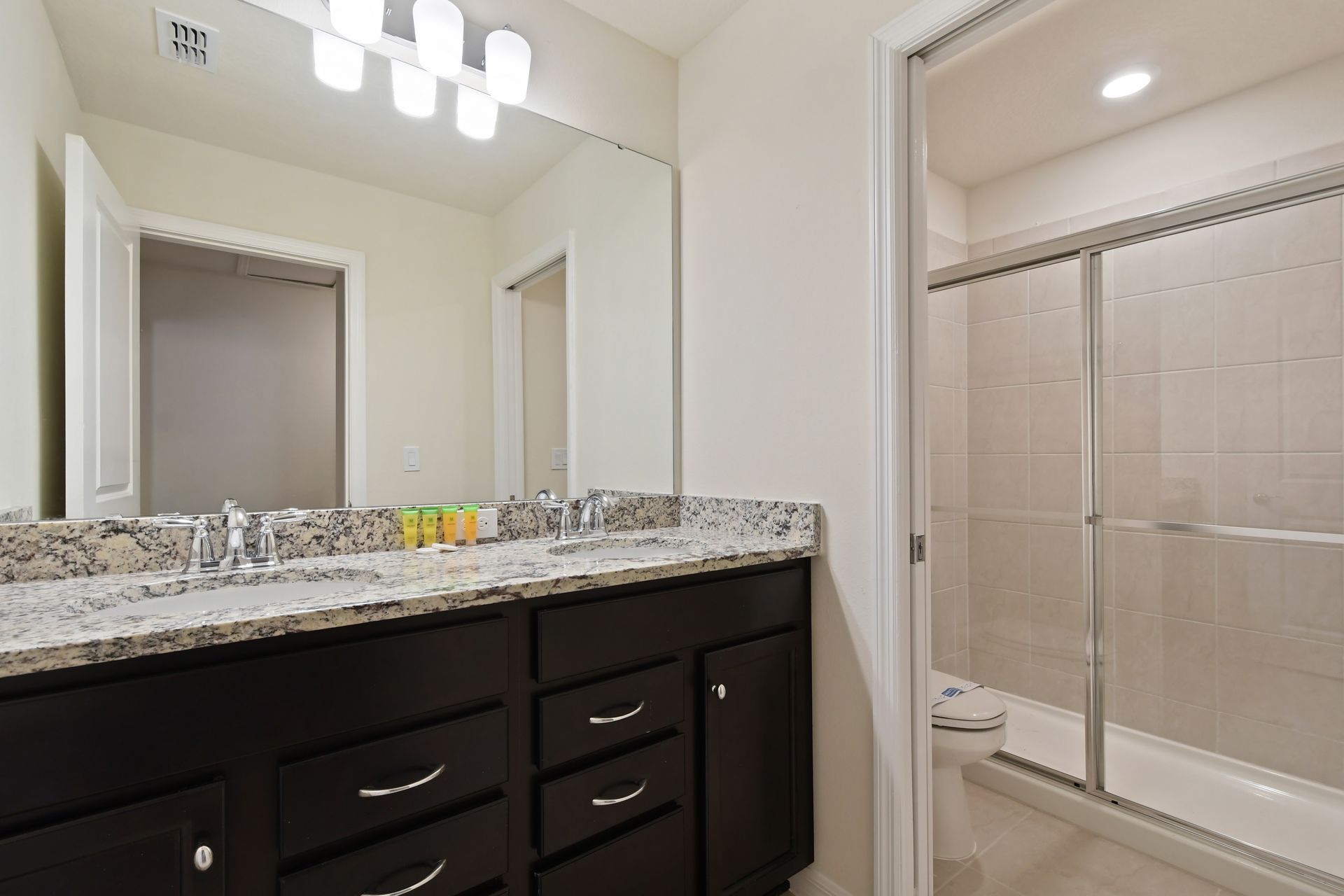 Bright bathroom with double granite vanity, glass shower, and modern lighting.
