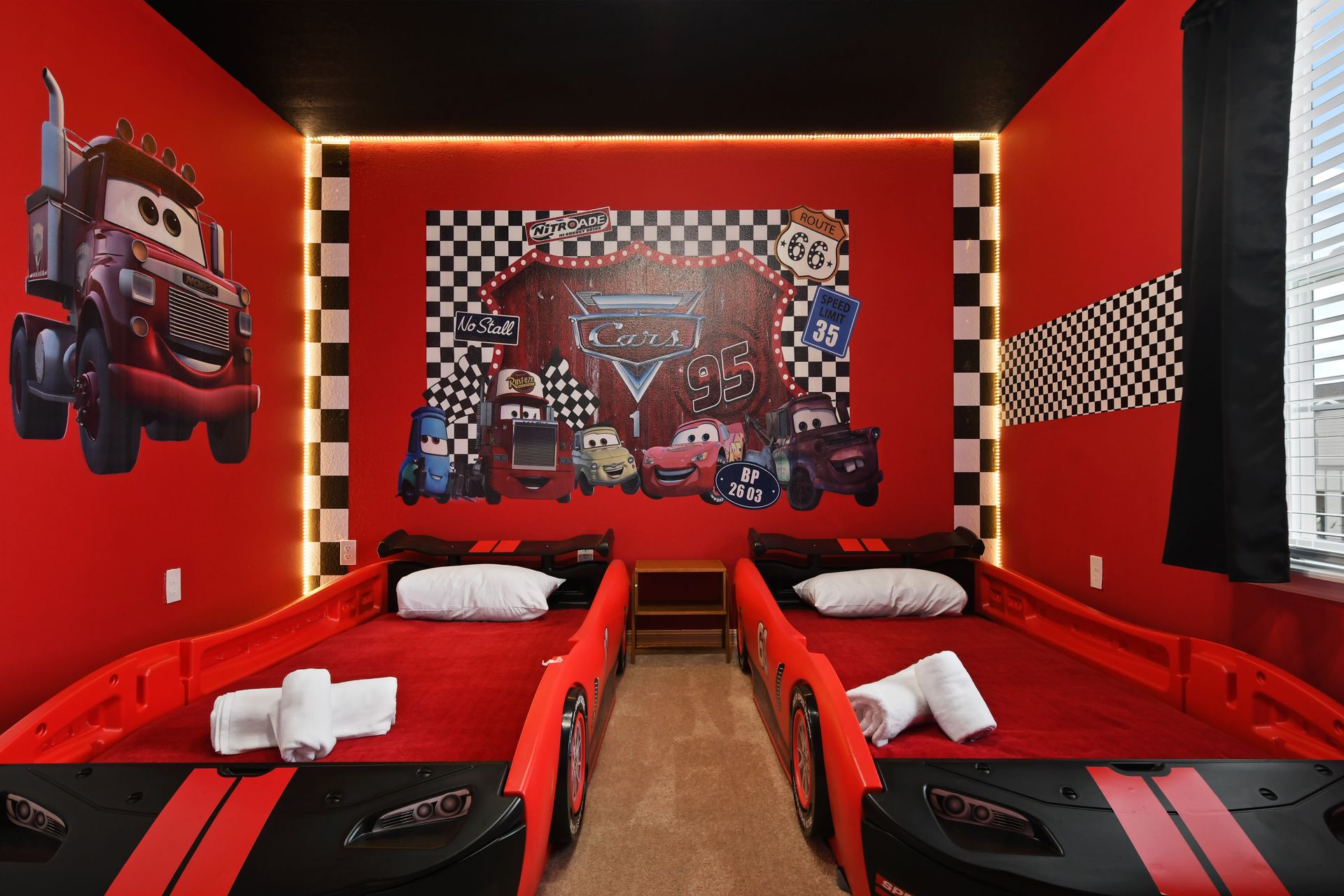 Race-themed kids’ room with twin car beds, bold red walls, and fun character art.
