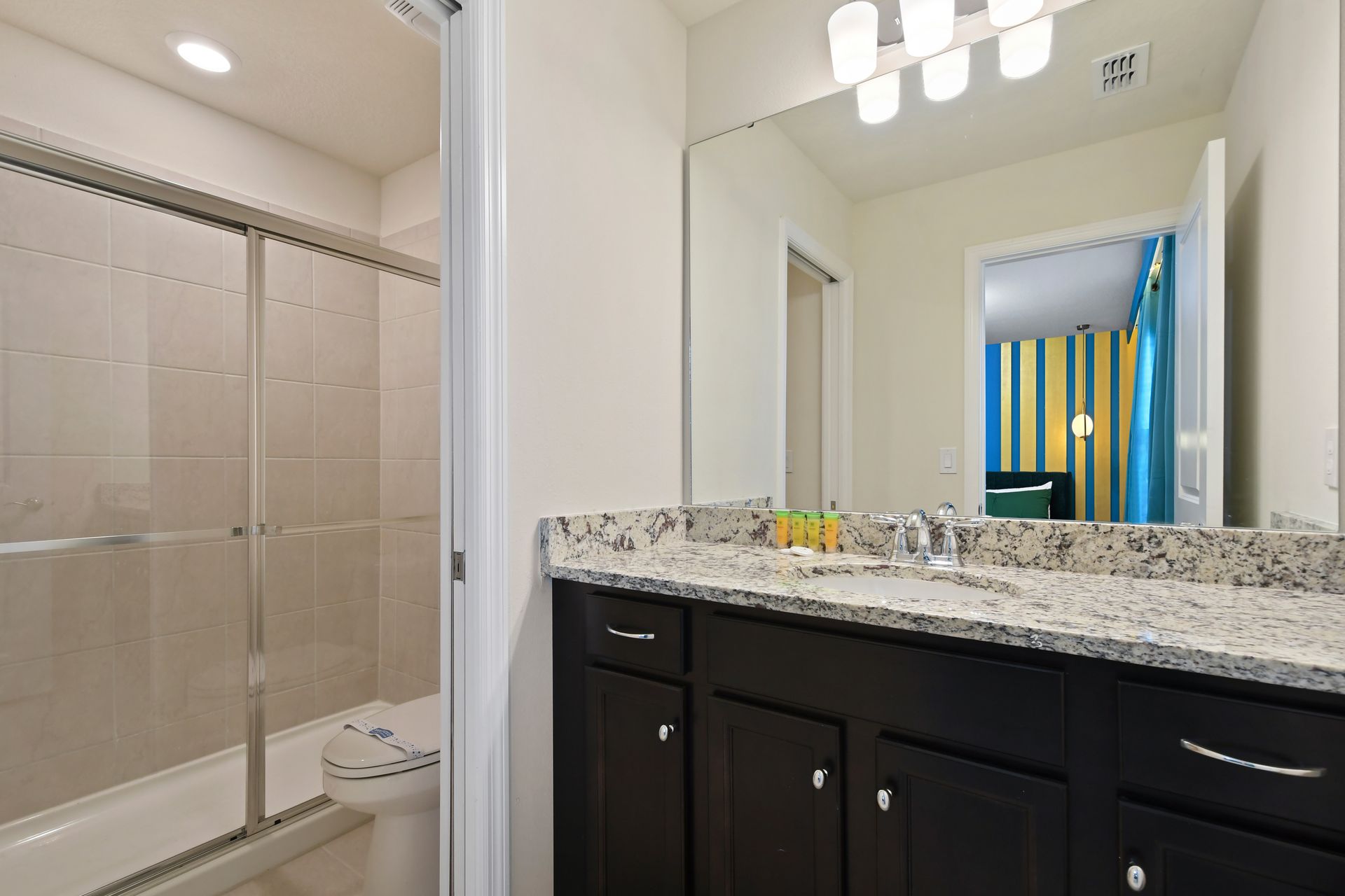 Modern ensuite bath with granite vanity, glass shower, and vibrant guestroom view.
