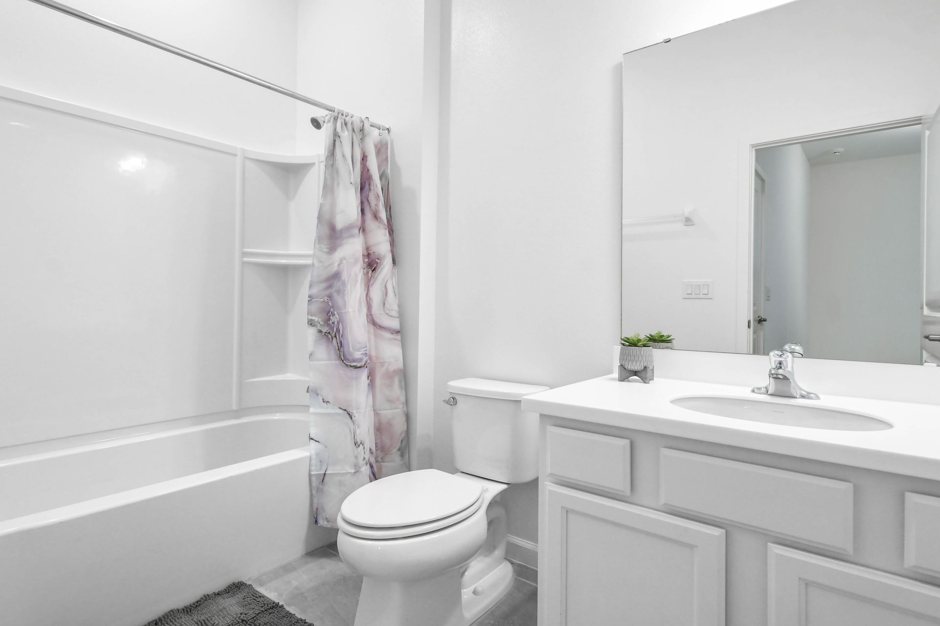 Modern bathroom with sleek white finishes, a large mirror, and a stylish shower curtain.