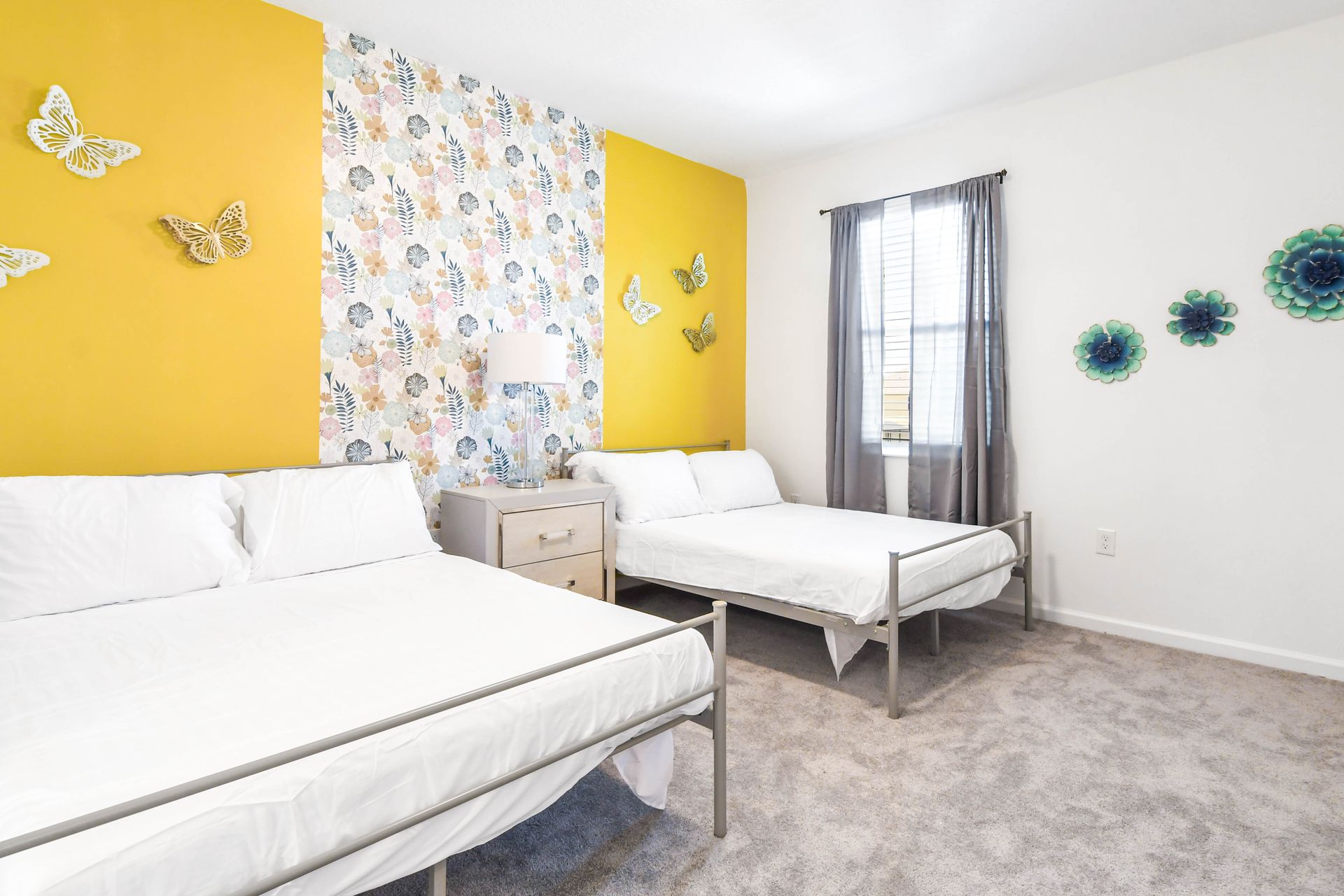 Bright and cheerful bedroom with two double beds, floral accents, and butterfly décor.
