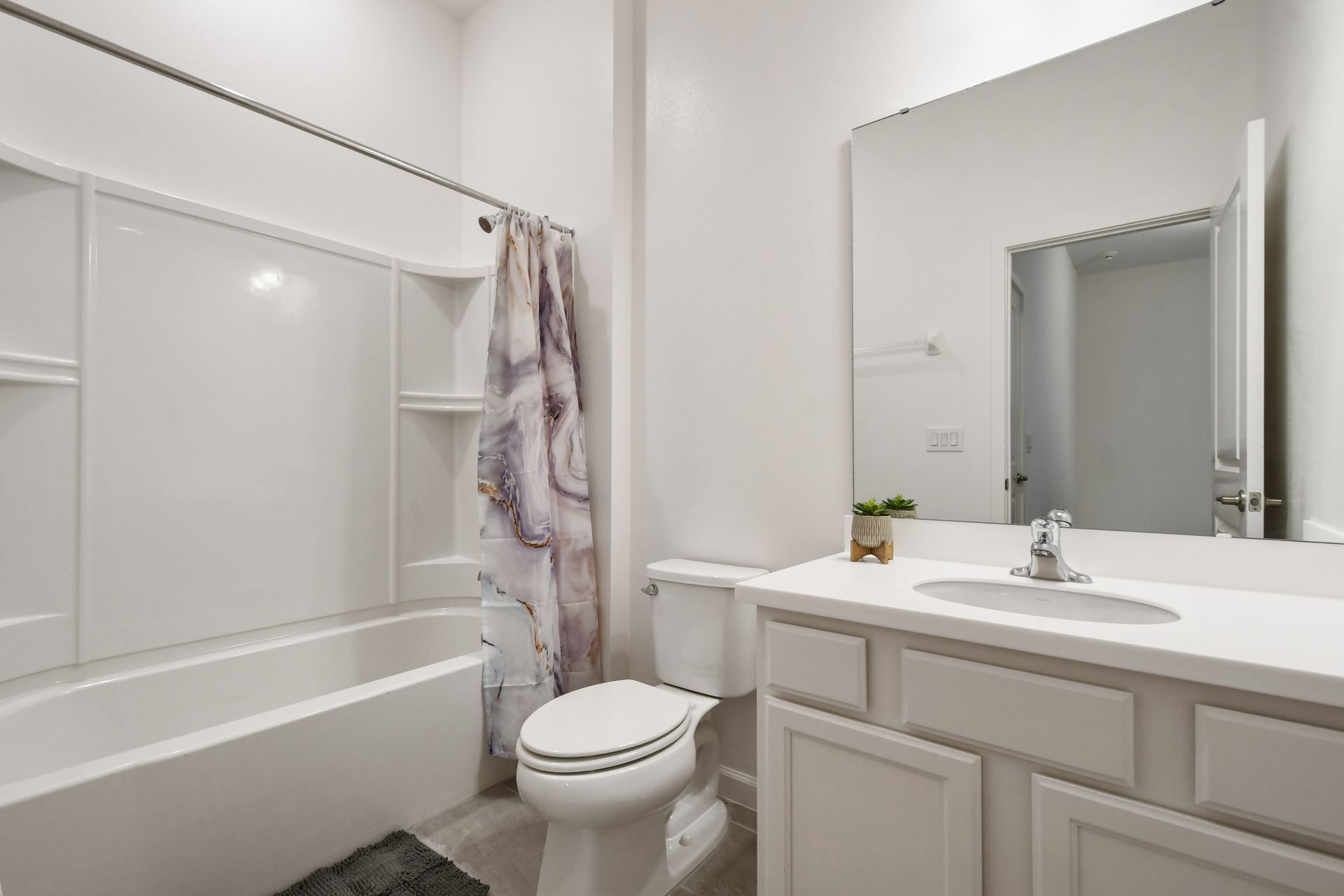 Modern and stylish bathroom with a sleek white vanity, large mirror, and tub-shower combo.