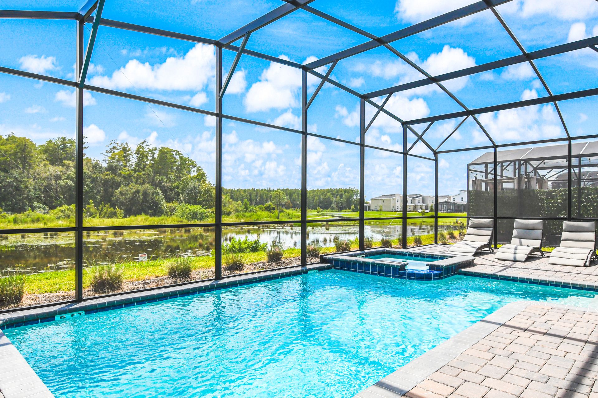 Screen-enclosed pool with a serene lake view, surrounded by lush greenery and sunny skies.