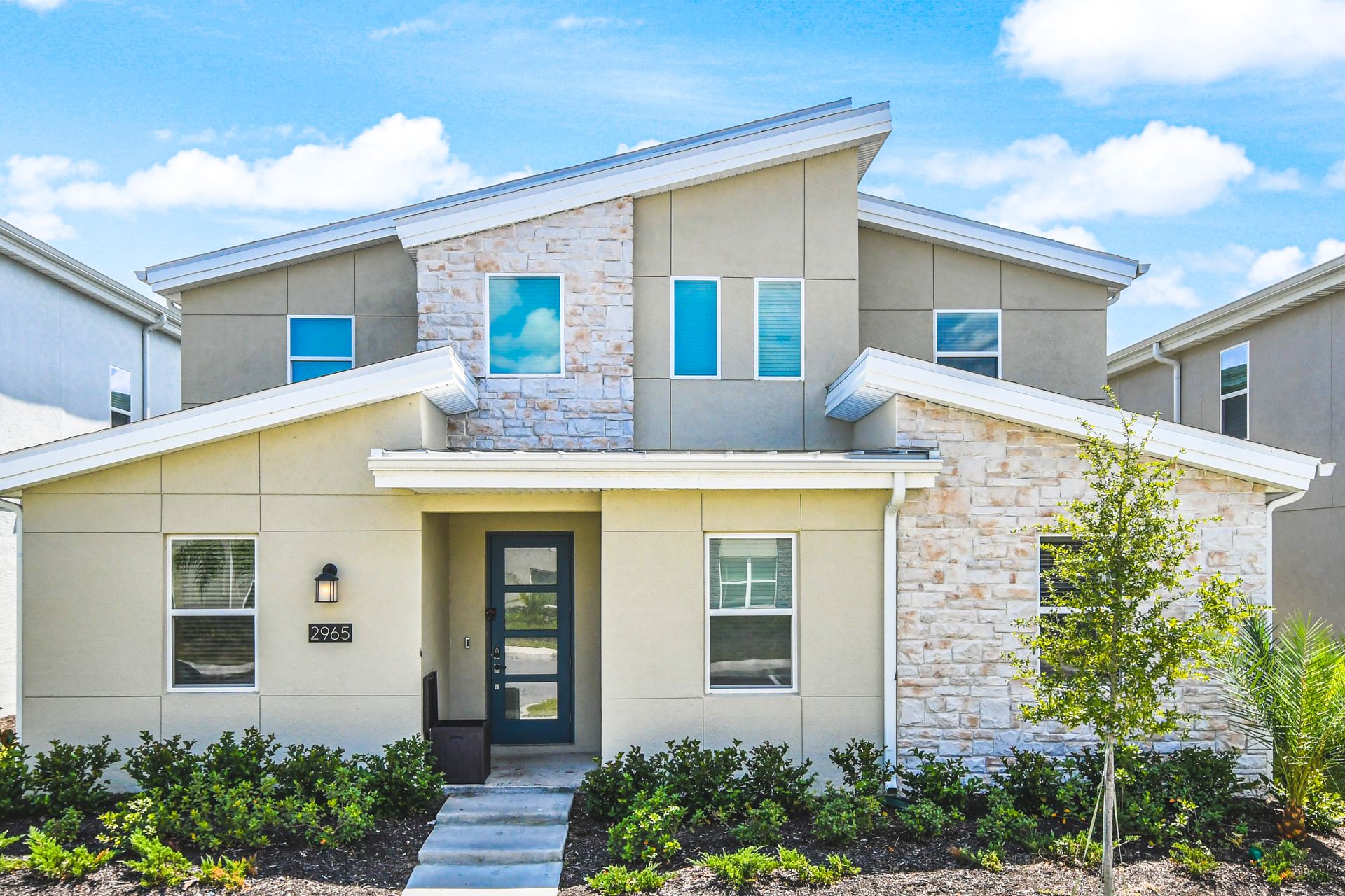 Modern two-story home with a stone-accented façade, sleek windows, and lush landscaping.