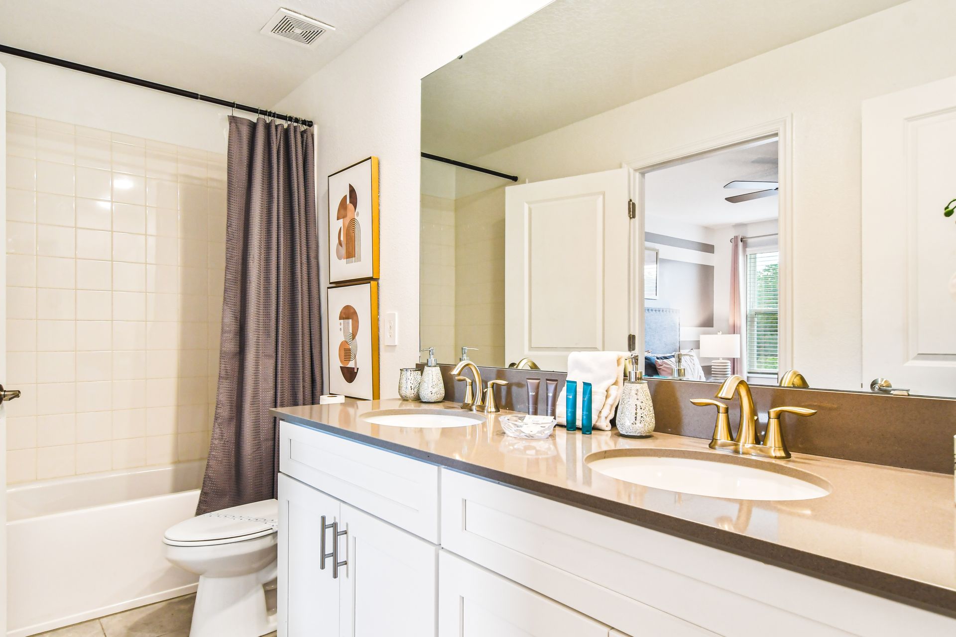 Bright bathroom with dual sinks, gold fixtures, a tiled shower, and chic decor accents.