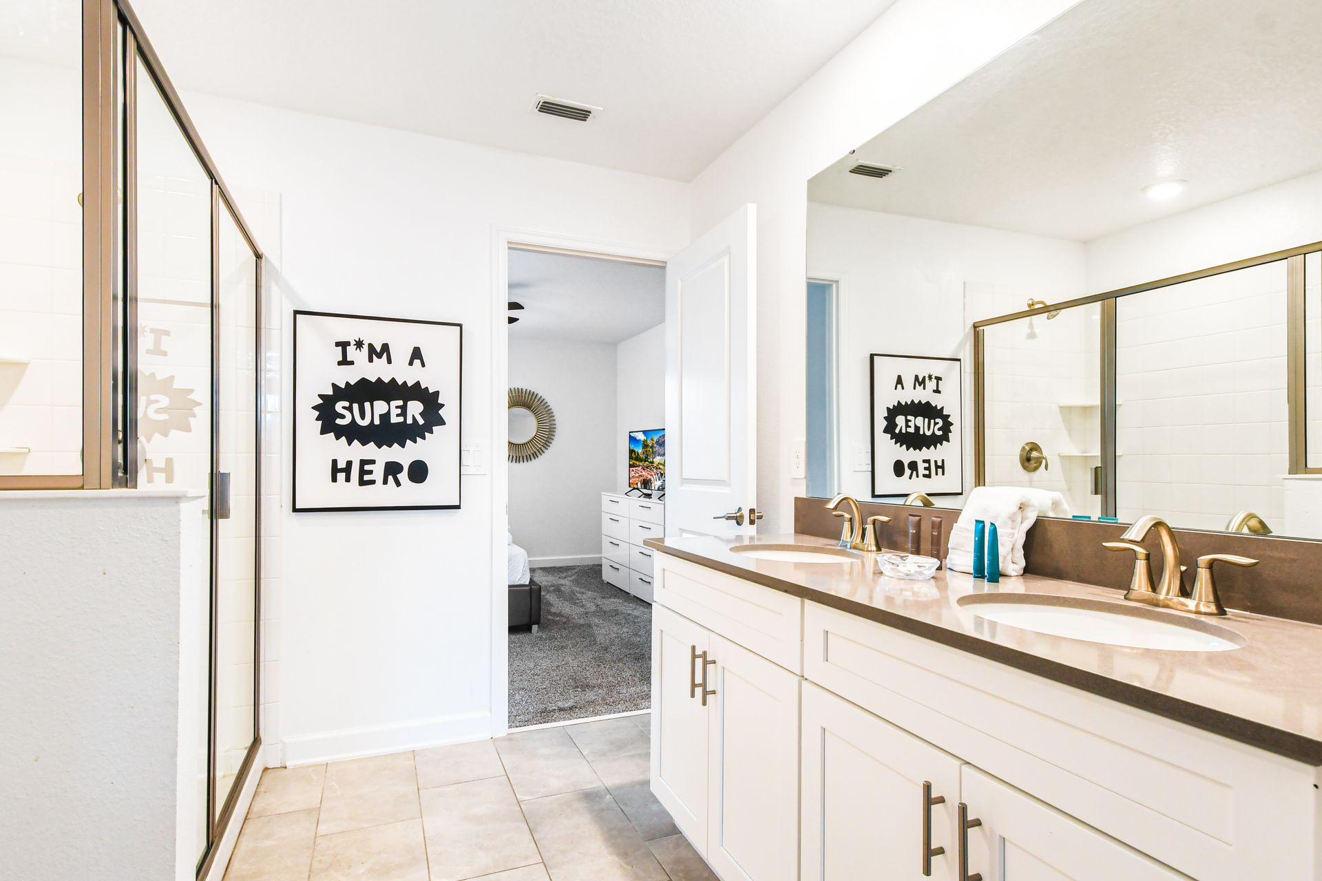 Bright and modern bathroom featuring a double vanity with gold fixtures, a large mirror, and a walk-in shower with glass doors.