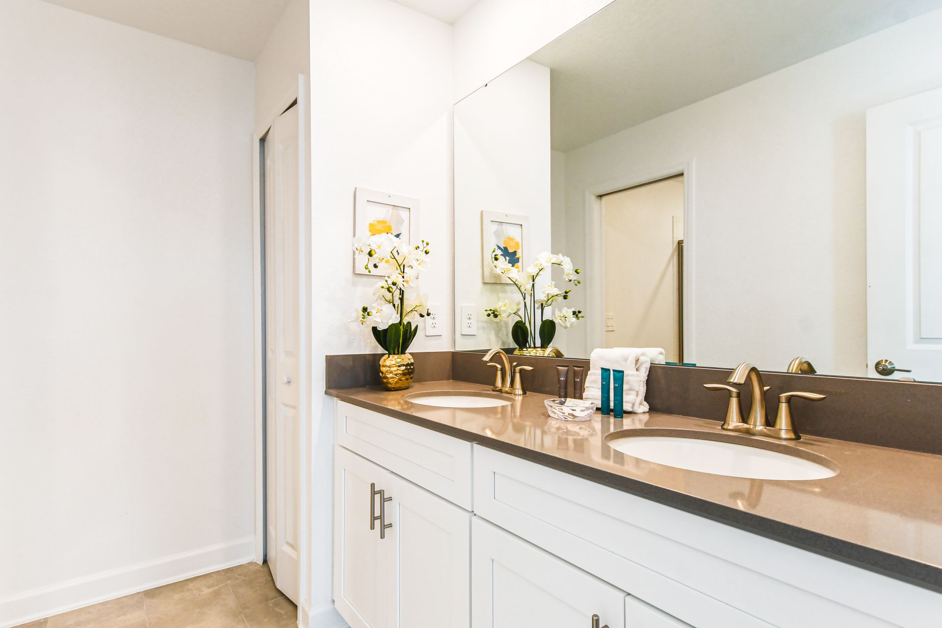 Elegant bathroom with a double vanity, gold fixtures, bright decor, and framed art.