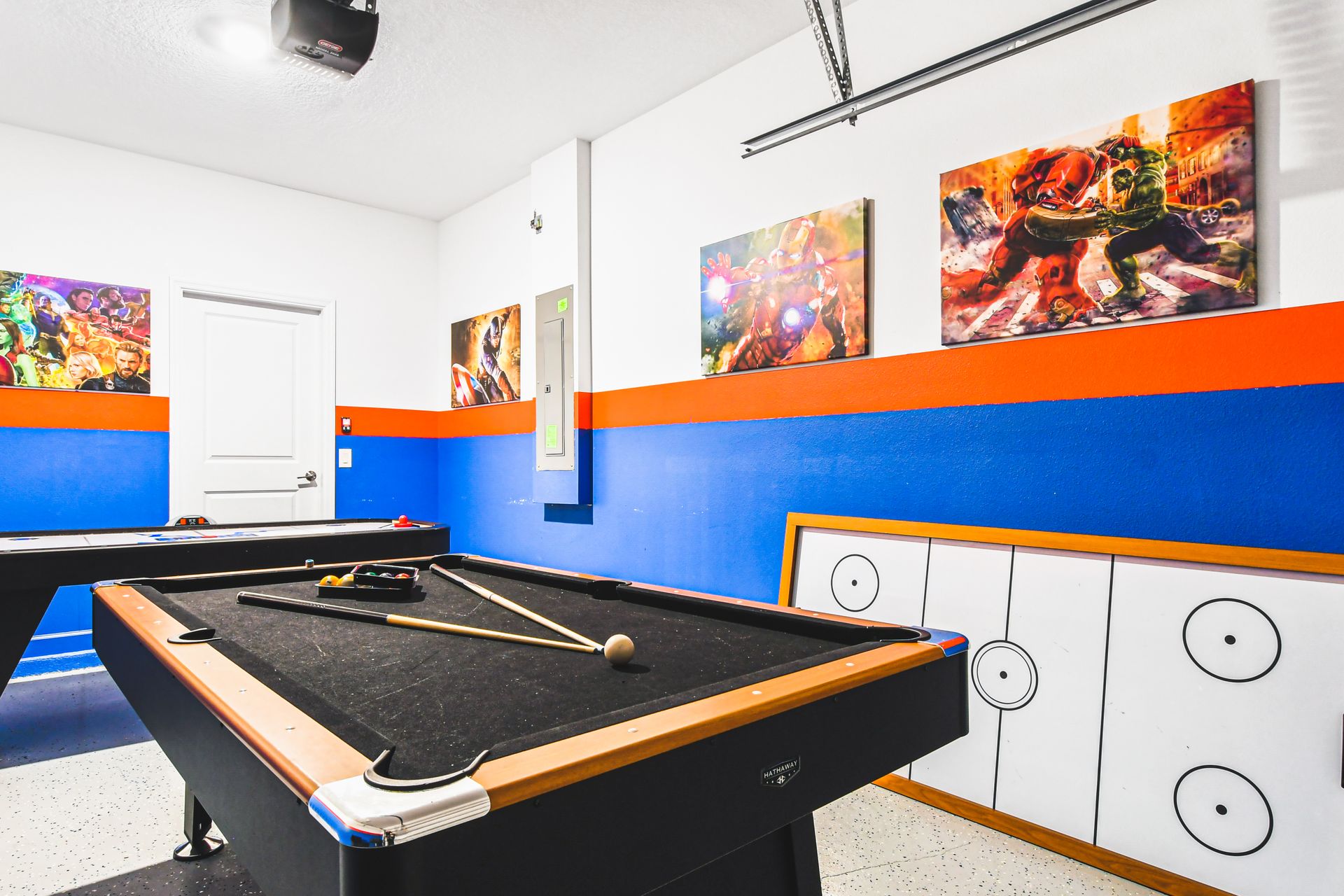 Colorful game room with pool, air hockey, bar stools, and superhero wall art