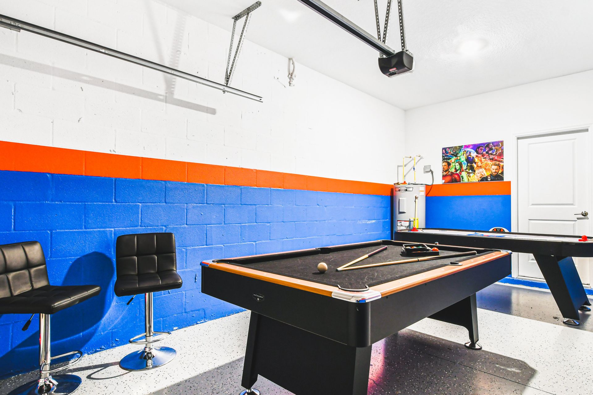 Colorful game room with pool, air hockey, bar stools, and superhero wall art