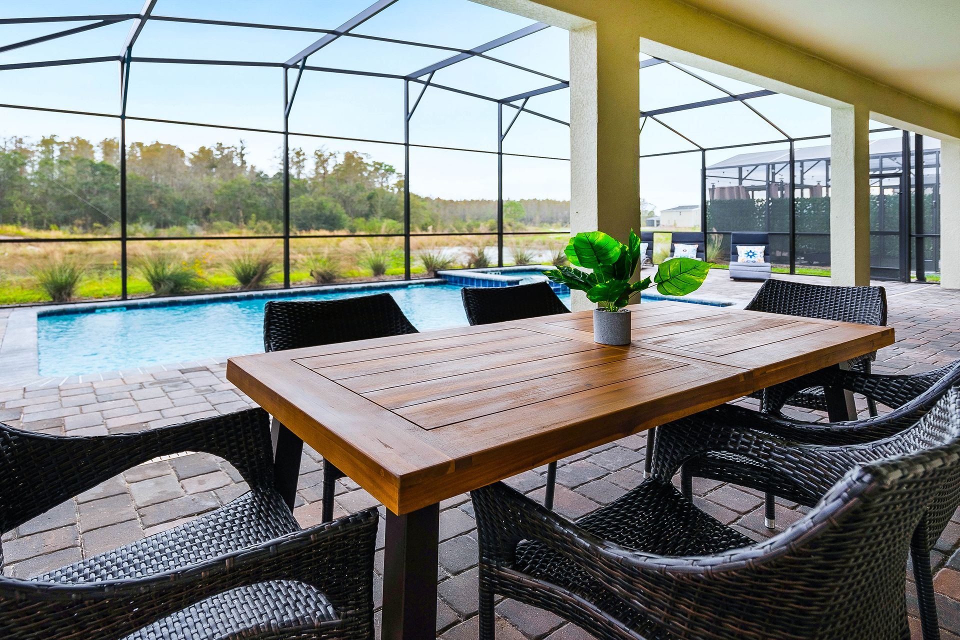Outdoor dining area with a wooden table and wicker chairs overlooking a serene pool.
