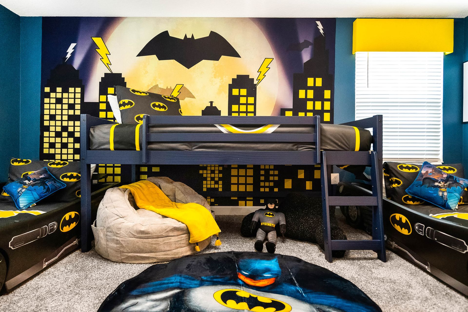 Batman-themed kids' room with cityscape mural, loft bed, Batmobile beds, and hero decor.